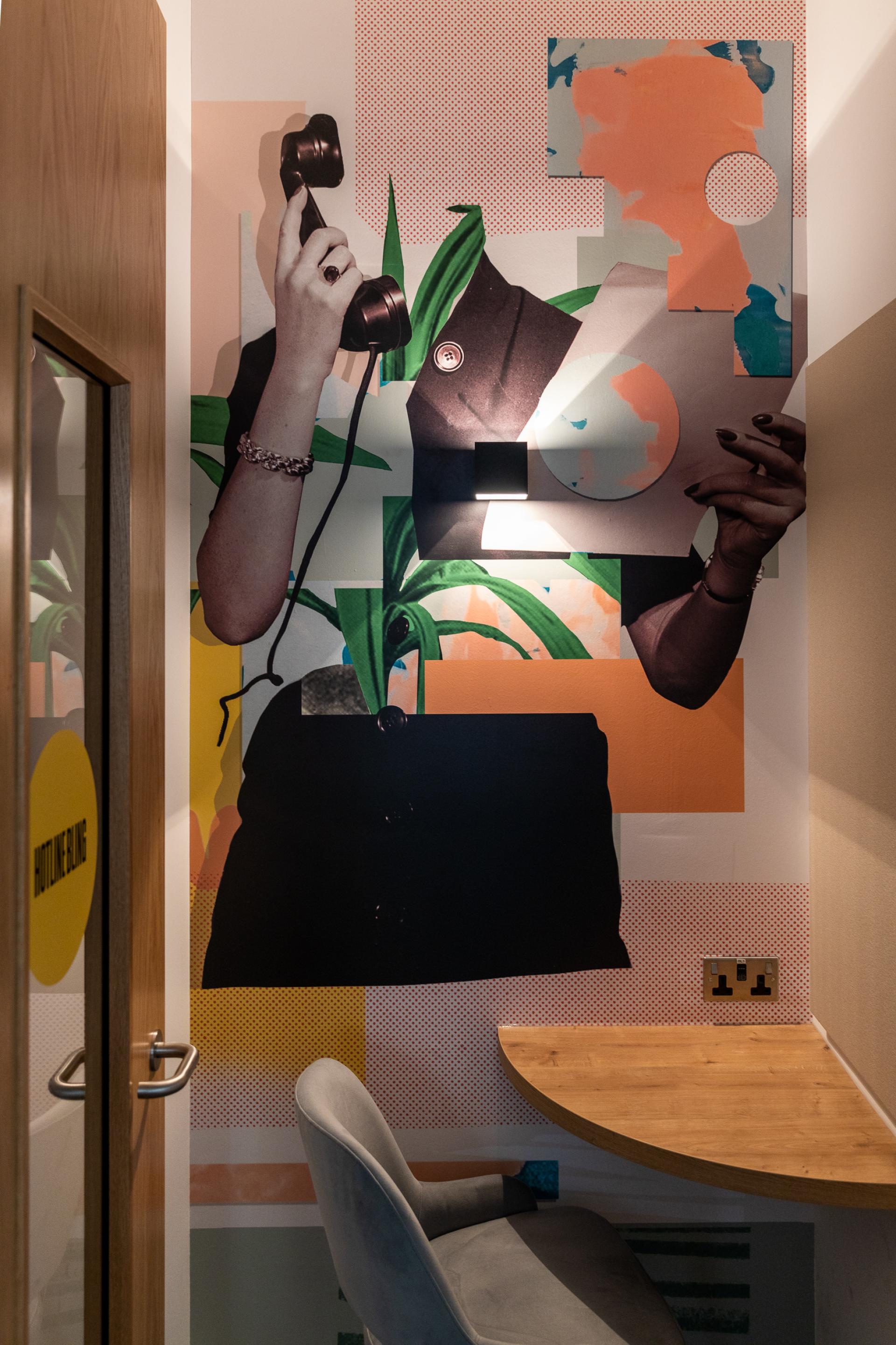Vibrant mural featuring a hand holding a phone, surrounded by bold patterns and colors in a cozy workspace.