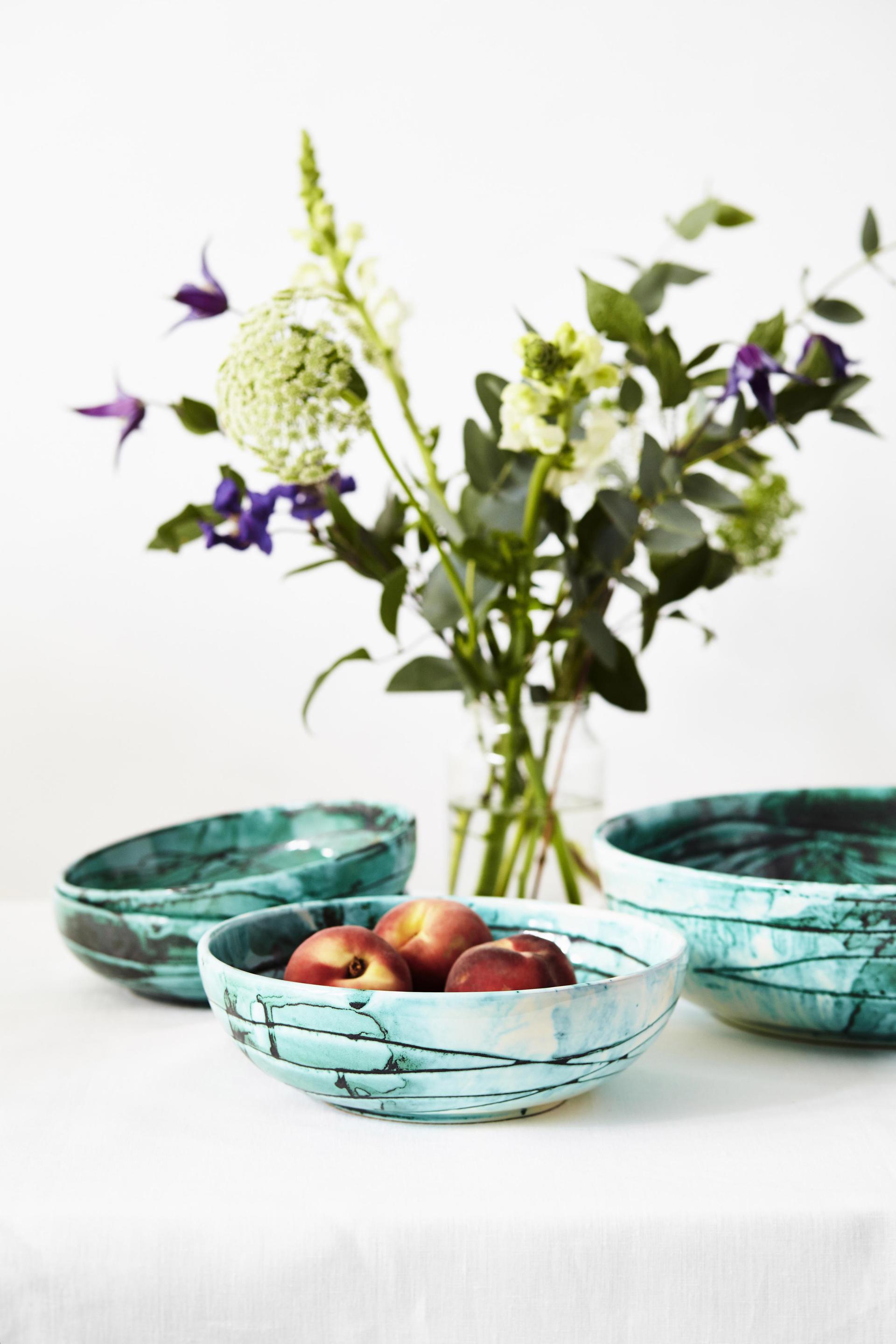 Colorful ceramic bowls filled with apples, complemented by a vase of fresh flowers on a table.