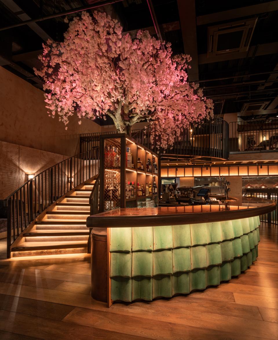 Elegant restaurant interior featuring a green bar design and a stunning cherry blossom tree, reflecting Chef Andrew Wong's new aesthetic.