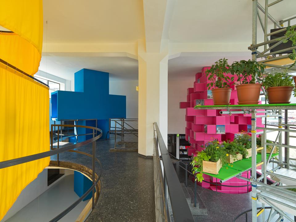 Colorful architectural installation by MVRDV featuring bright blue and pink structures, incorporating greenery and contemporary design elements.