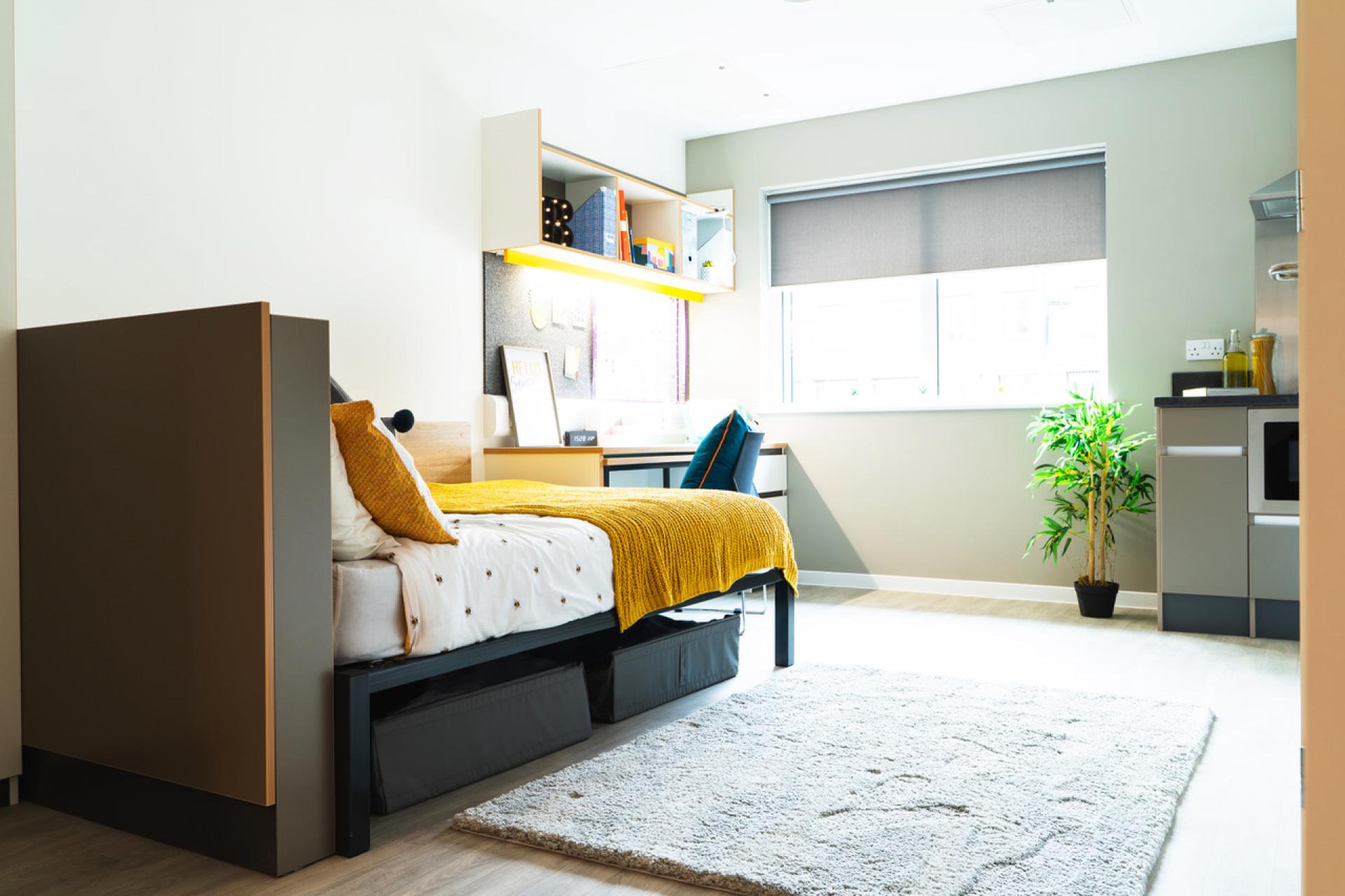 Modern student accommodation interior in Birmingham featuring a cozy bed, study area, and natural light.