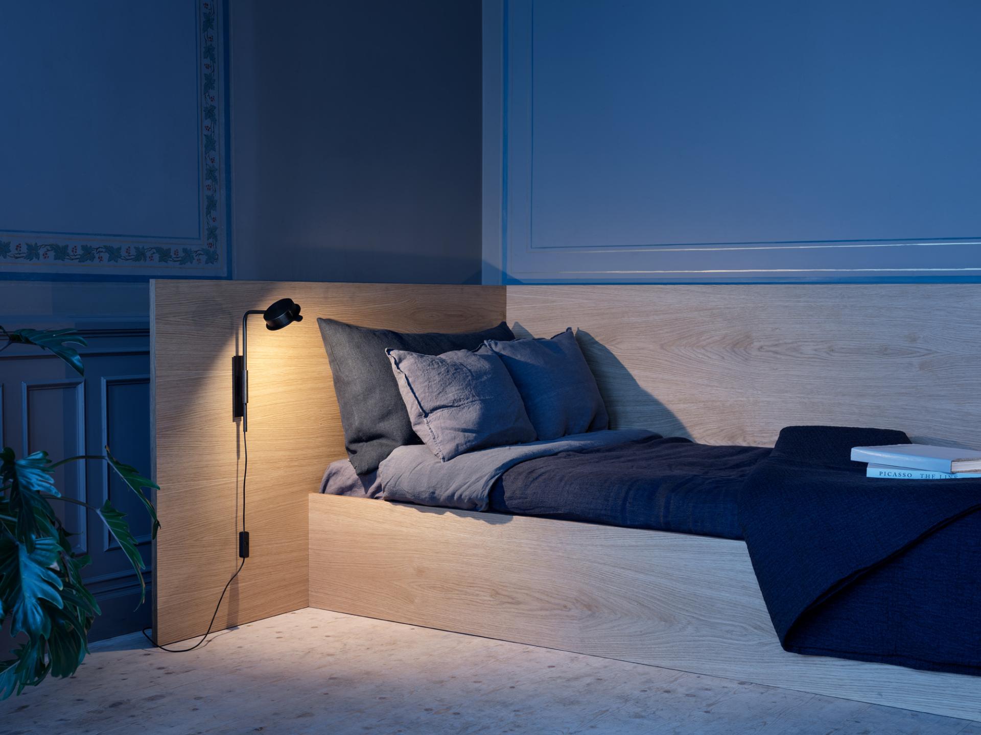 Elegant bedroom featuring the w102 Chipperfield lamp by Wästberg, illuminating a minimalist wooden bed and cozy bedding.