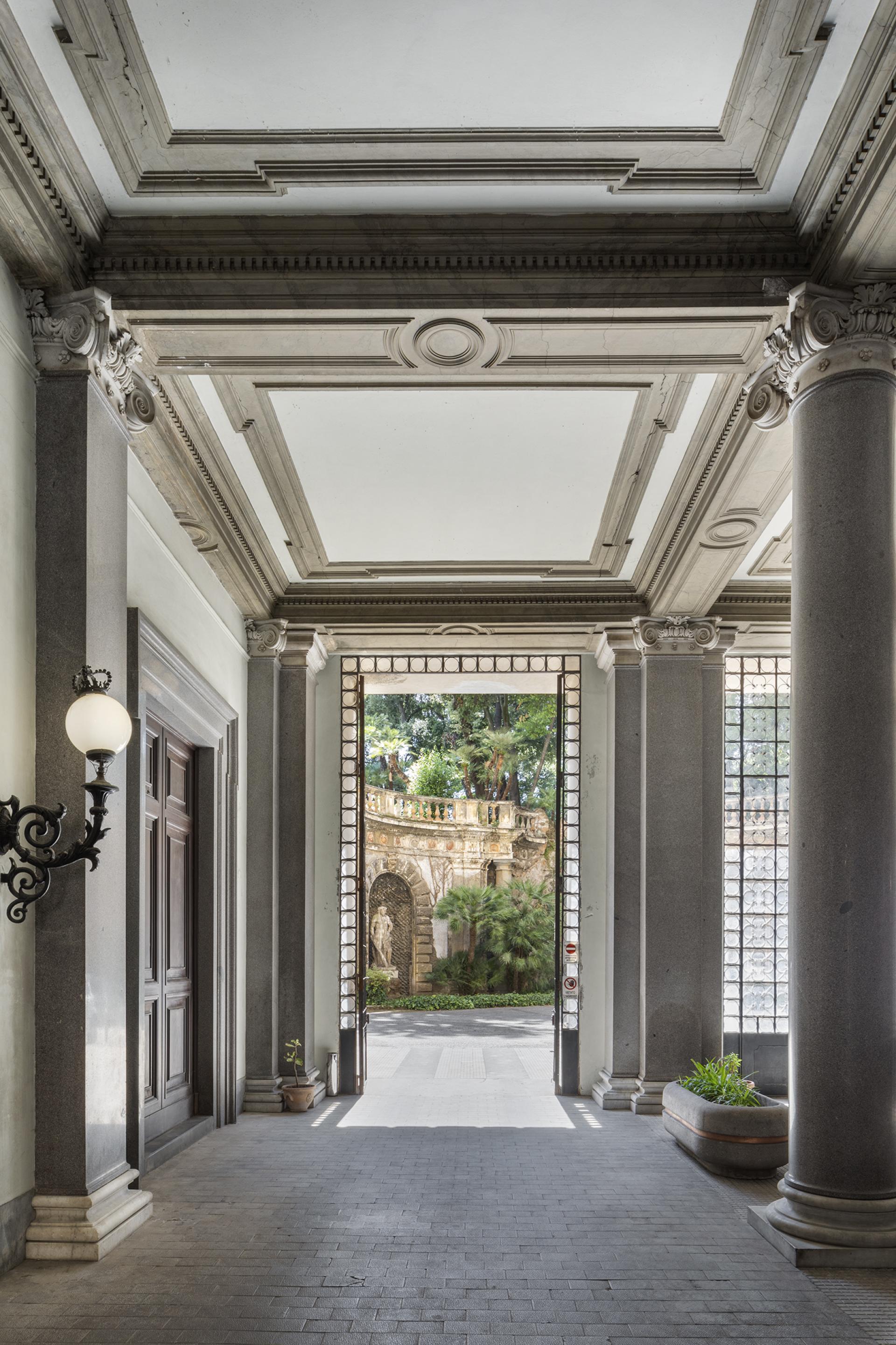 Elegant entrance of Palazzo Brancaccio, showcasing classic architecture and a glimpse of the lush garden outside.