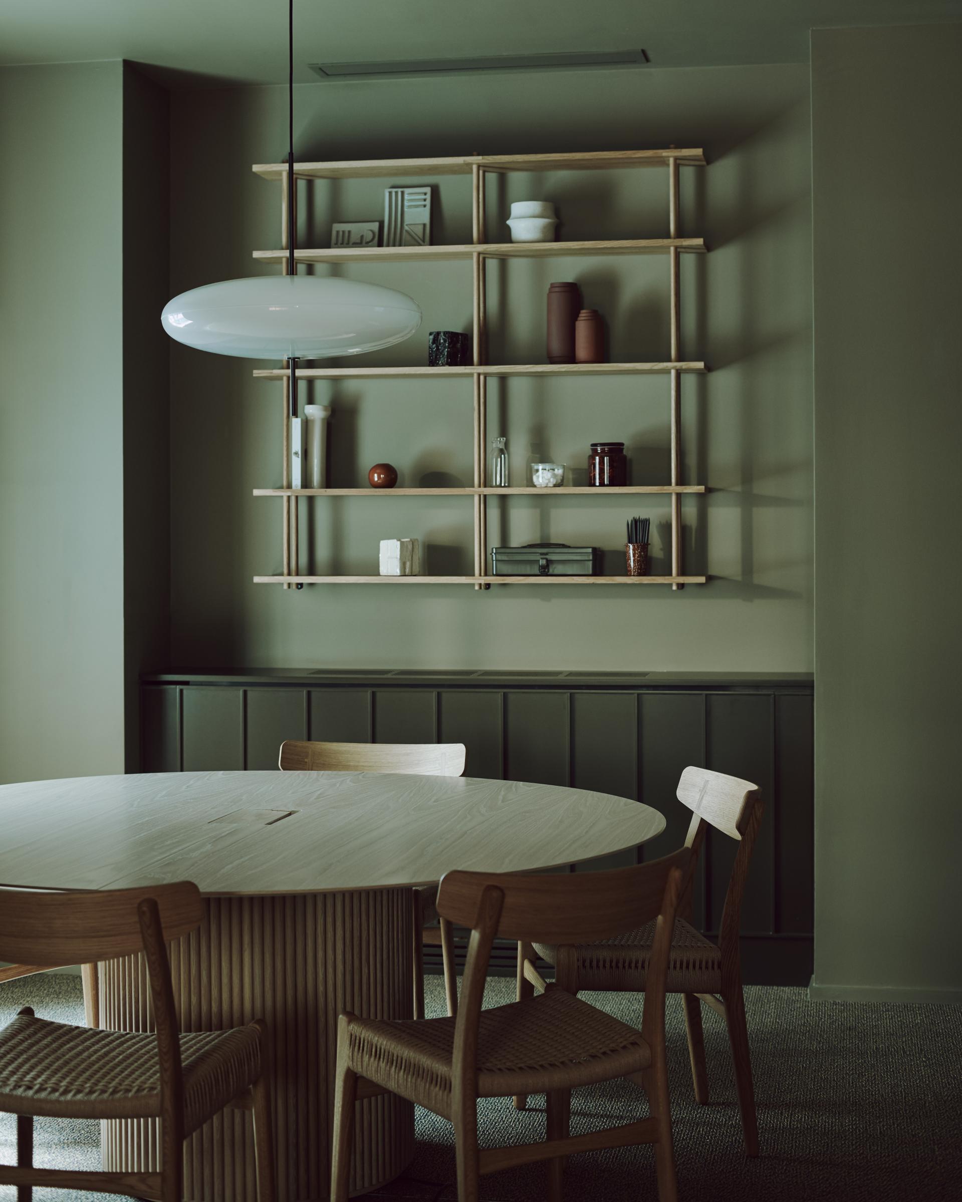 Calm workspace interior featuring a round wooden table surrounded by chairs, with an organized shelving unit above.