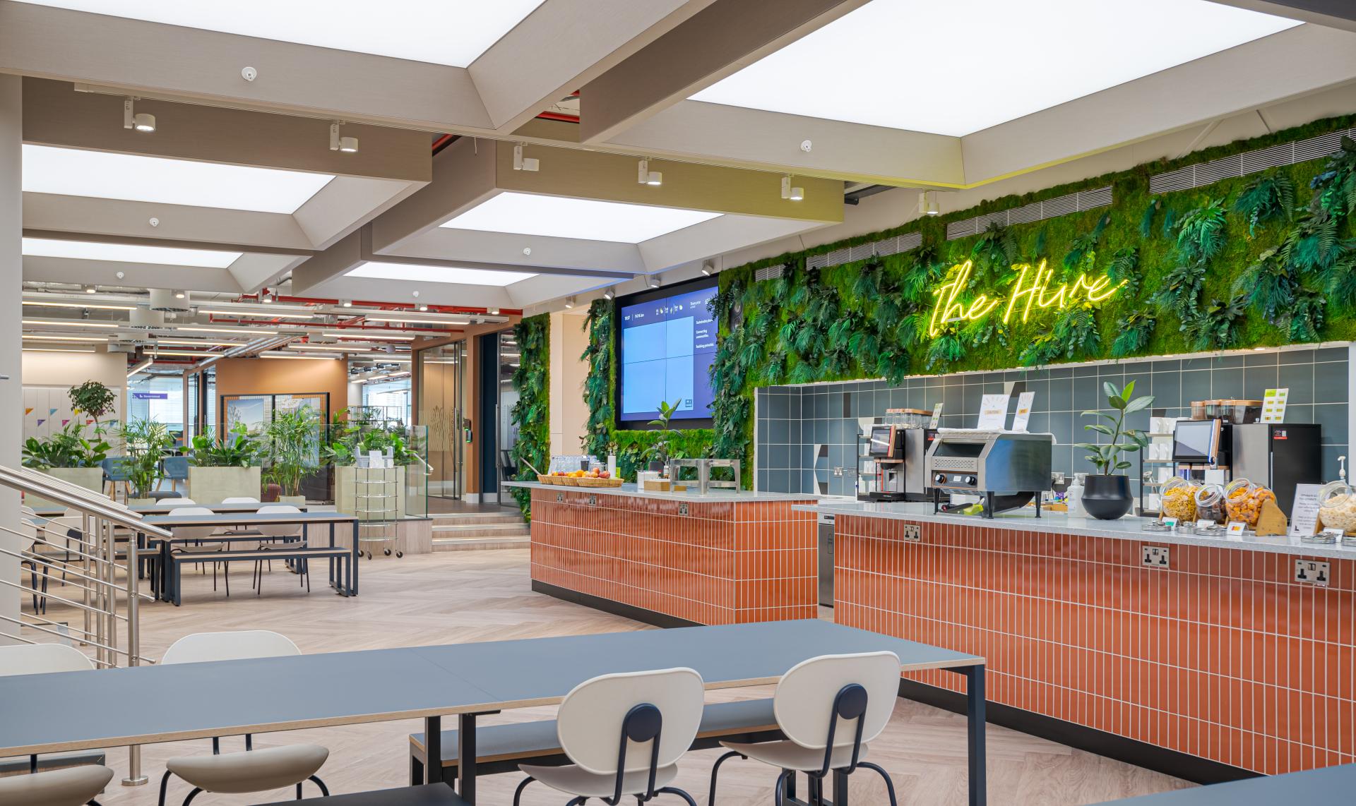 Vibrant workspace at Landsec’s headquarters featuring The Hive café, green plants, and collaborative seating areas.