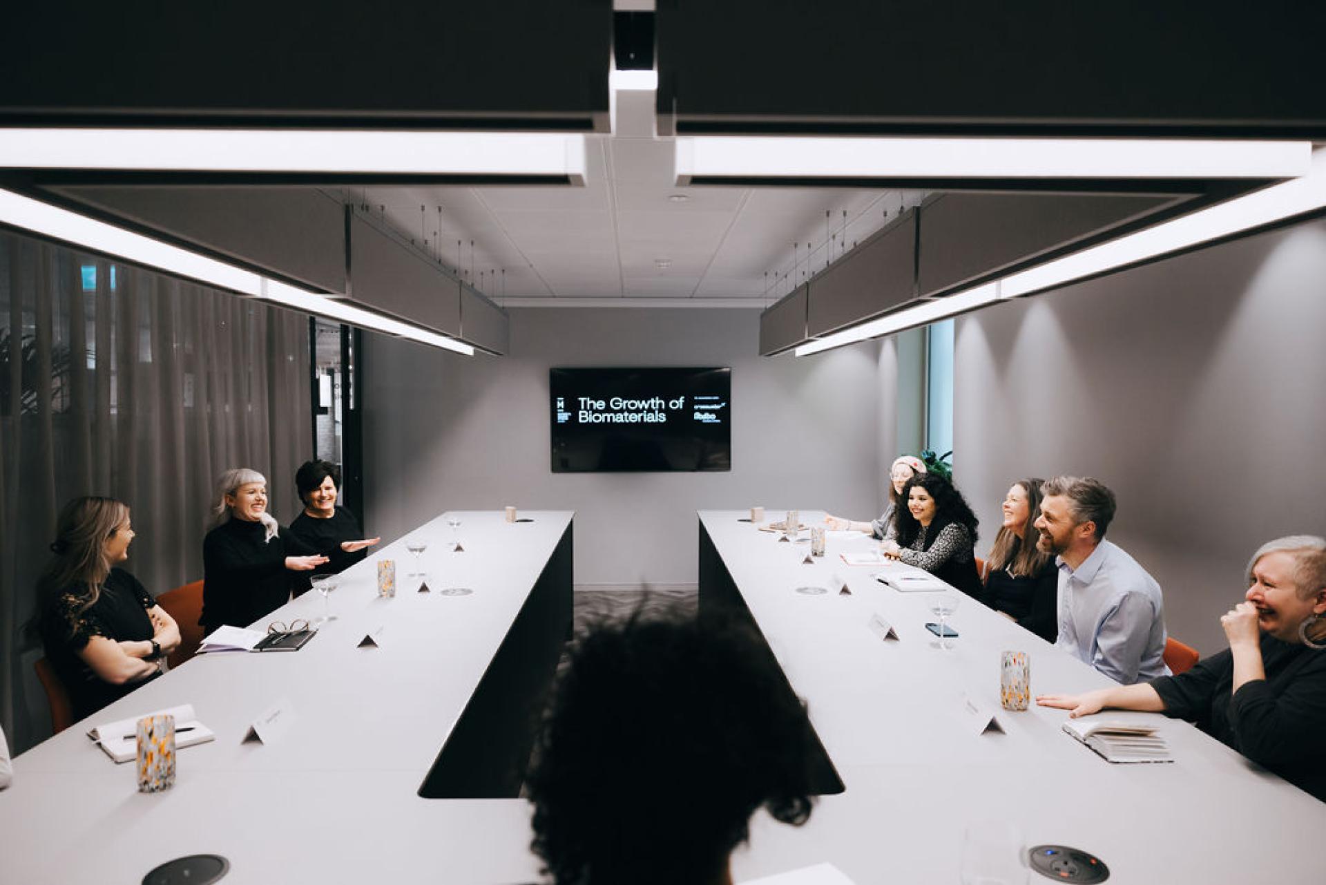 Discussion on biomaterials taking place in a modern conference room with engaging participants and a presentation screen.