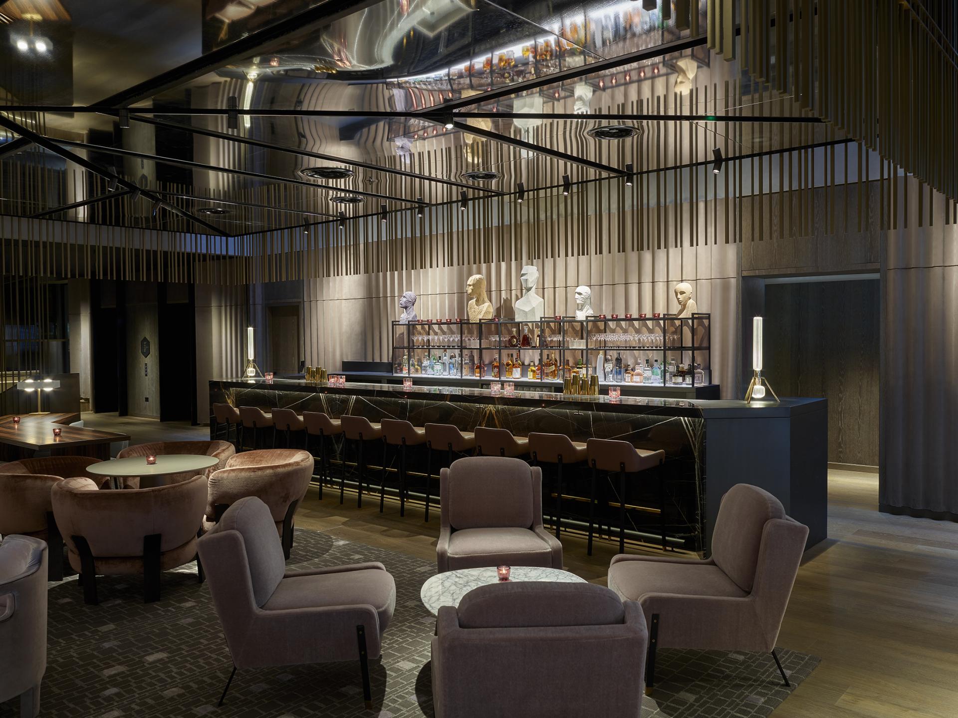 The stylish bar area of a Leicester Square hotel features plush seating and artistic sculptures, reflecting Yabu Pushelberg's theatrical design.