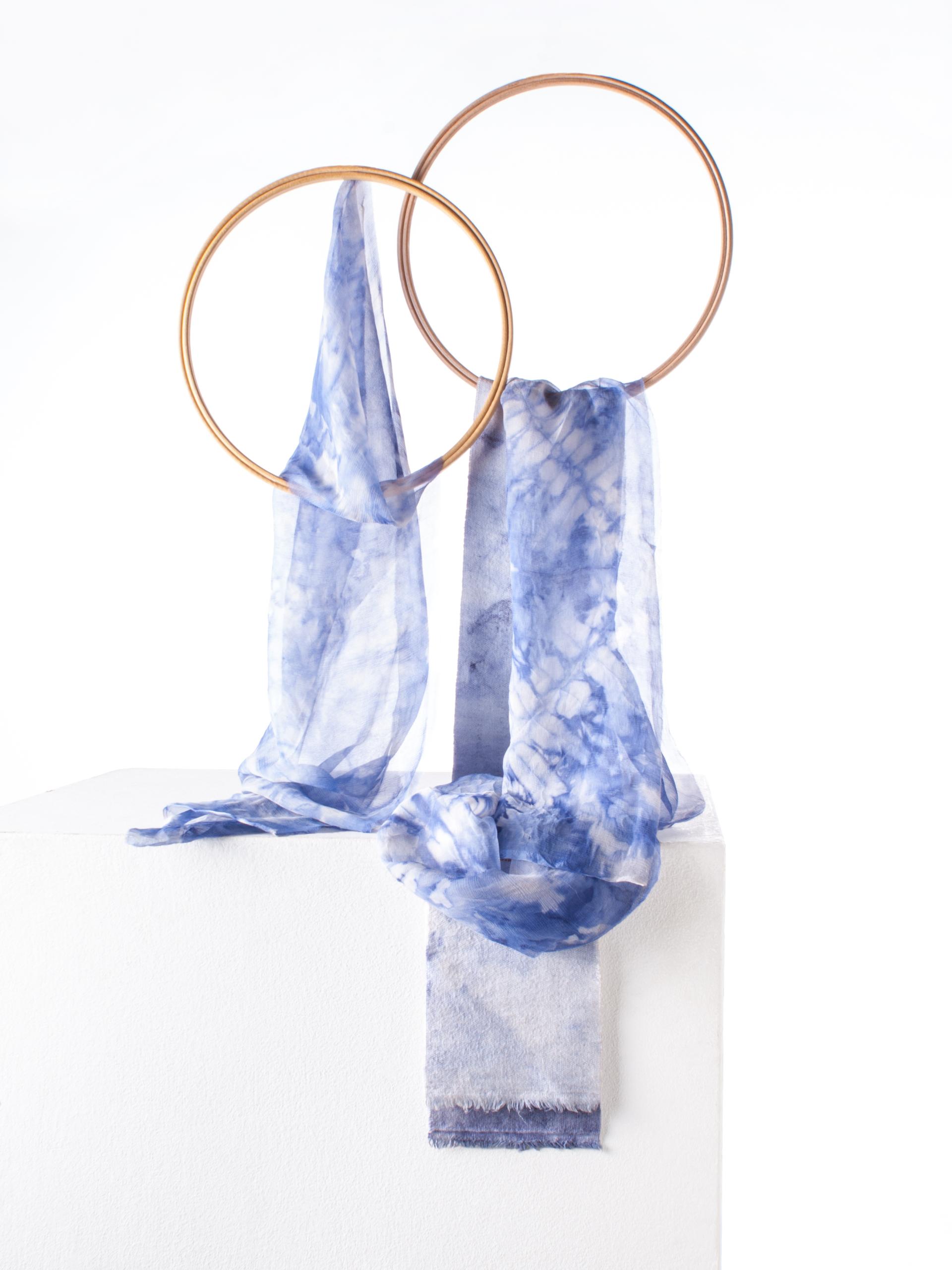 Elegant blue tie-dyed textiles hanging on circular copper rings, showcasing innovative biodesign in textile artistry.