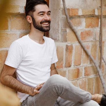 Hasan Roomi smiling while sitting against a brick wall, reflecting Dubai's vibrant café culture and design philosophy.