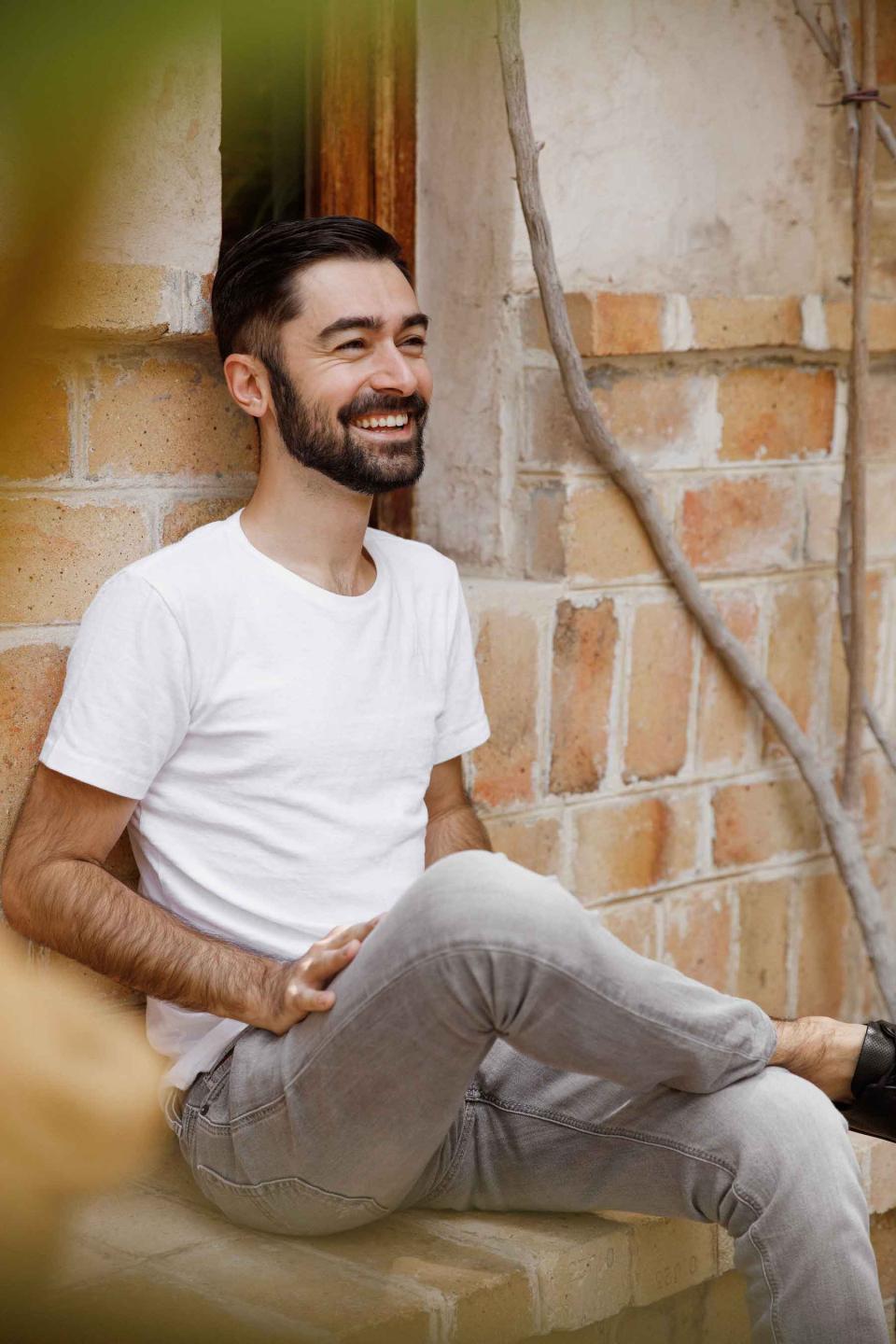 Hasan Roomi smiling while sitting against a brick wall, reflecting Dubai's vibrant café culture and design philosophy.