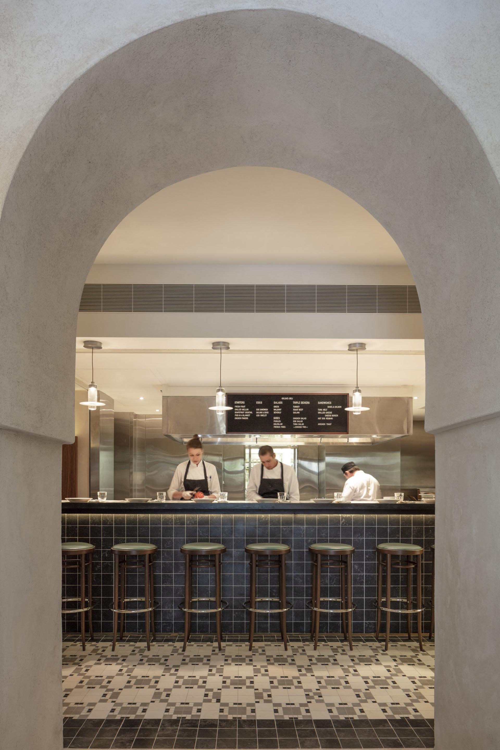 Minimalist kitchen design at The Jaffa featuring chefs, bar stools, and a contemporary menu board, reflecting John Pawson's style.