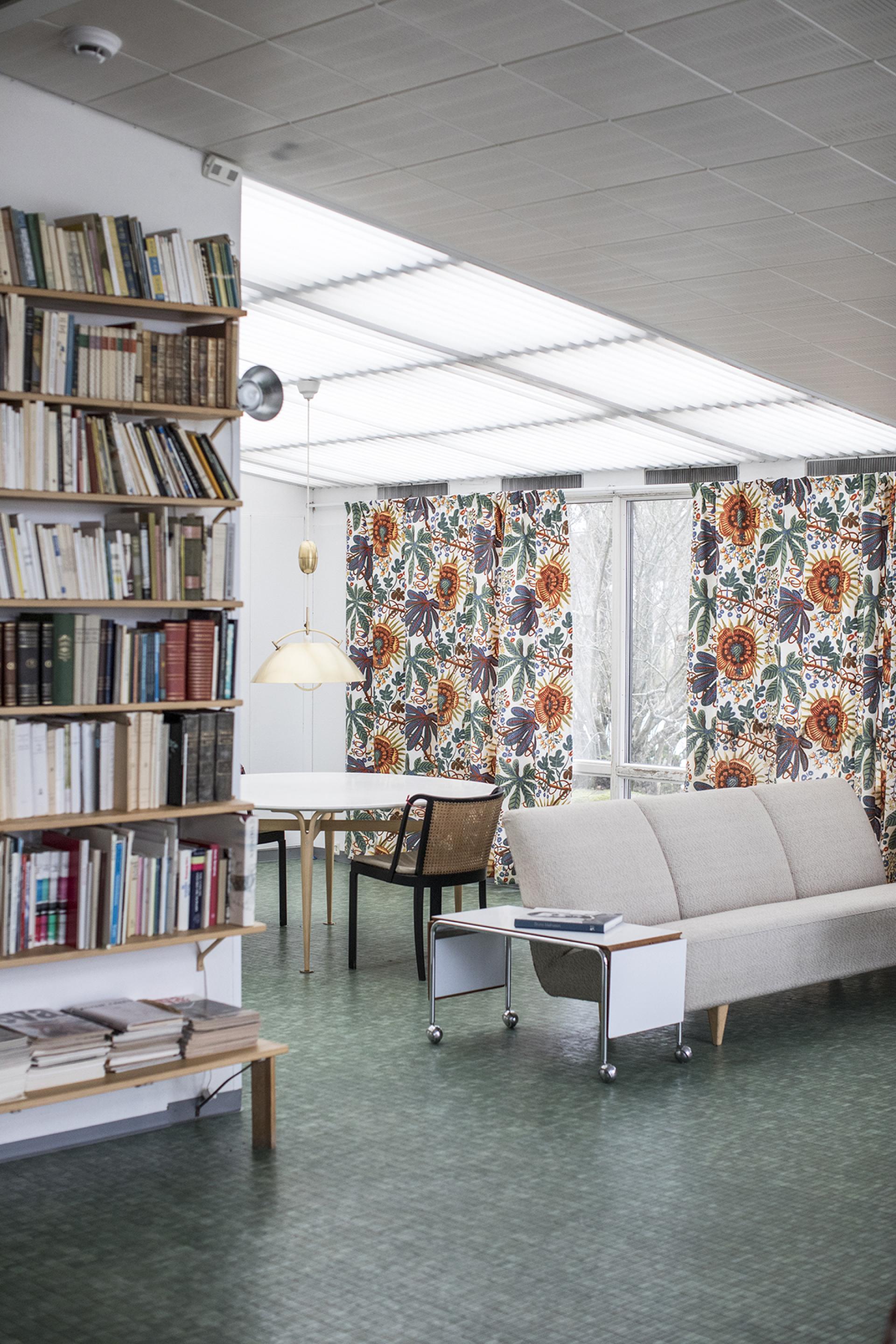 Modern living space in Södra Kull featuring vibrant floral curtains, a cozy sofa, bookshelves, and a dining area.