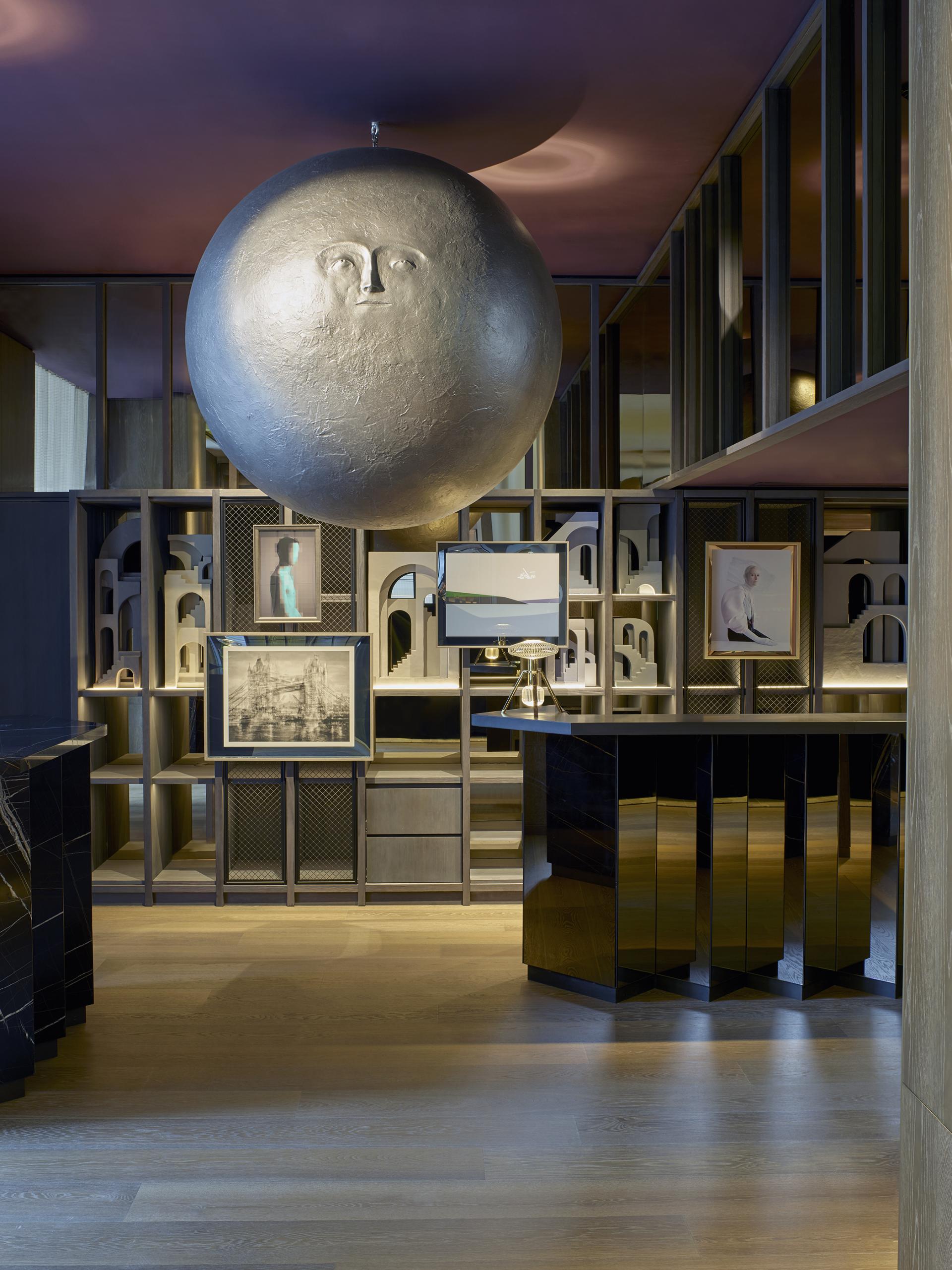 Theatrical hotel interior featuring a large sculptural face light fixture, unique artwork, and sleek furniture design.