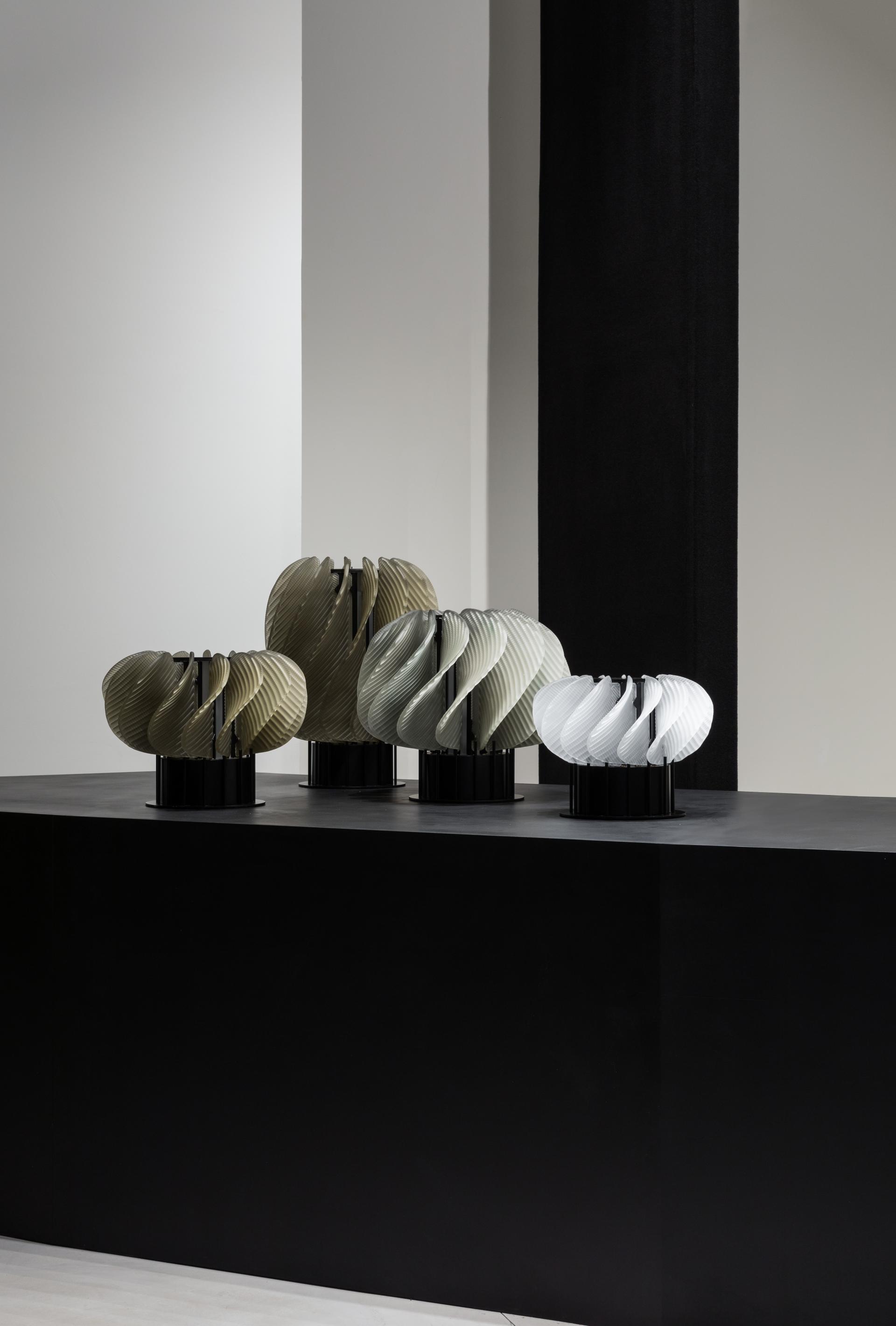 Elegant lighting sculptures in various colors showcased on a sleek black display at WonderGlass's new London showroom.