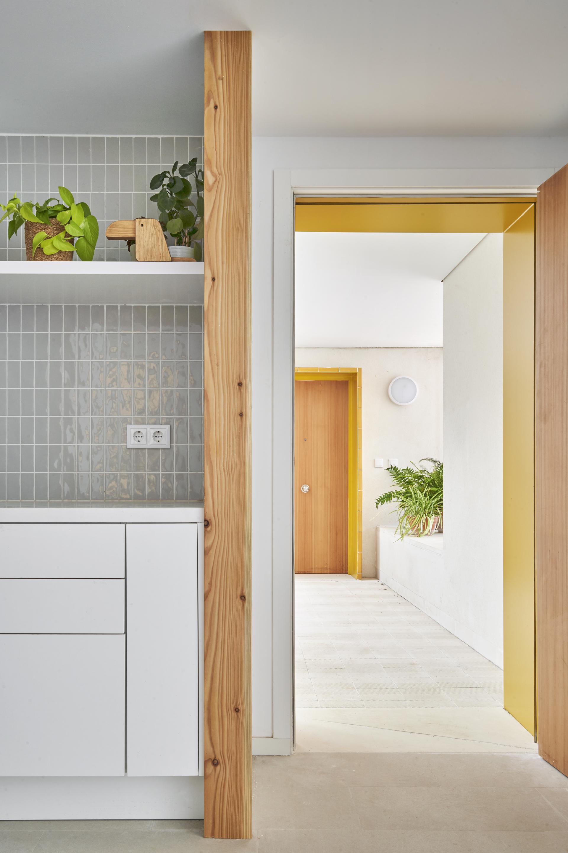 Modern kitchen with ceramic tiles, wooden accents, and a door leading to a vibrant hallway with plants.
