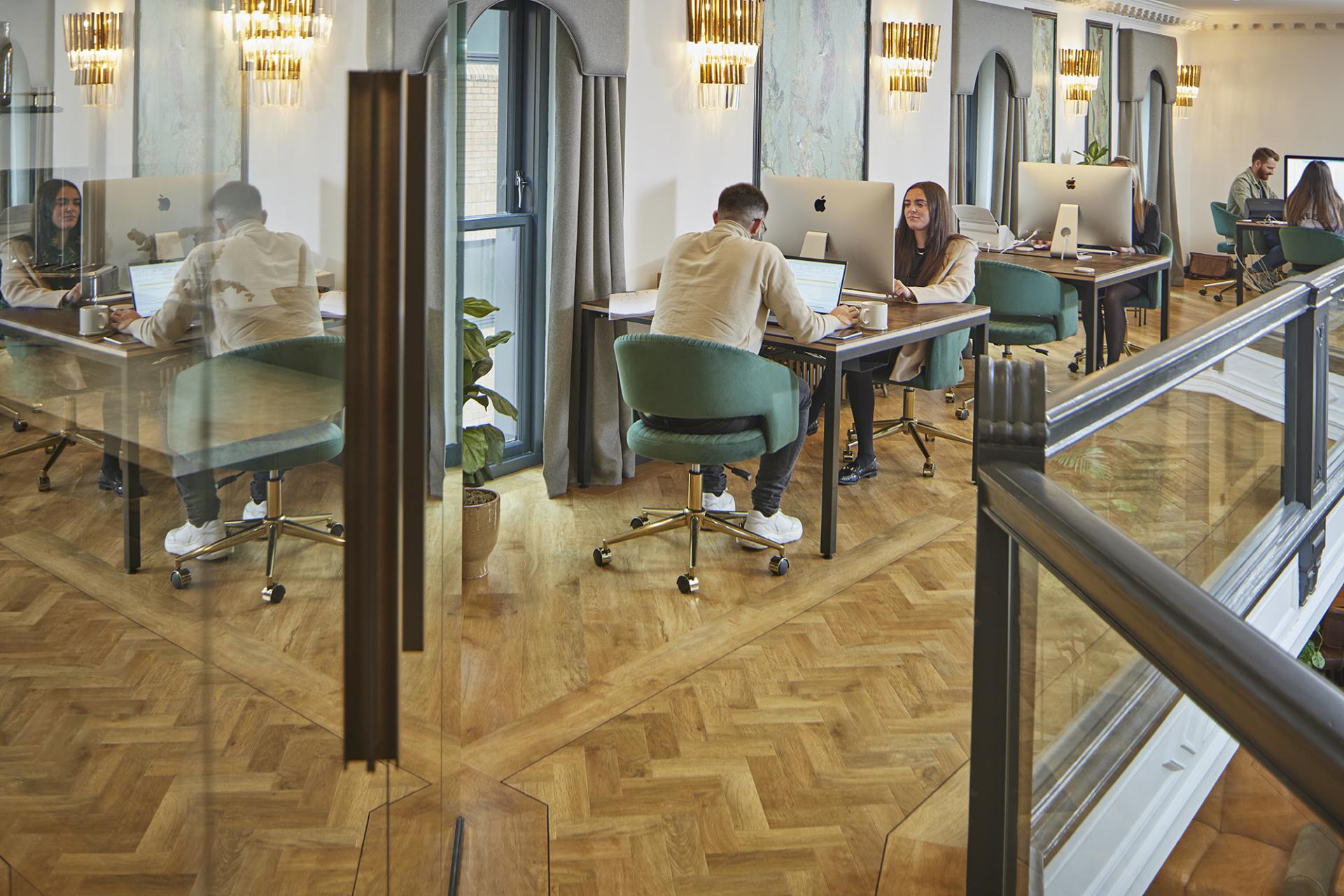 Modern workspace featuring Karndean Designflooring, showcasing individuals collaborating over custom-designed flooring in a historic building.