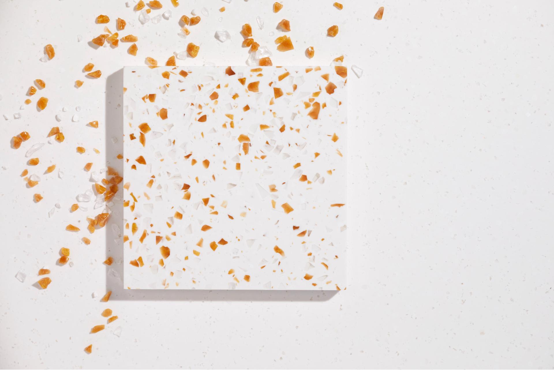 Textured white surface featuring vibrant orange and clear flecks, showcasing Surface Matter's circular Material Rescue initiative.