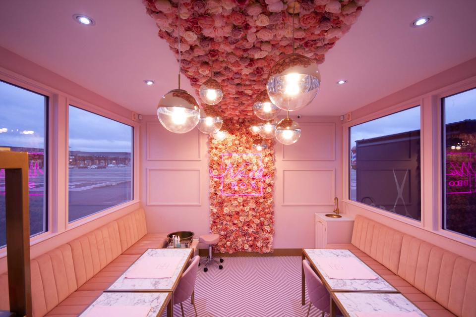 Chic pastel pink interior with floral wall, stylish lighting, and modern tables at Nailbox nail salon.
