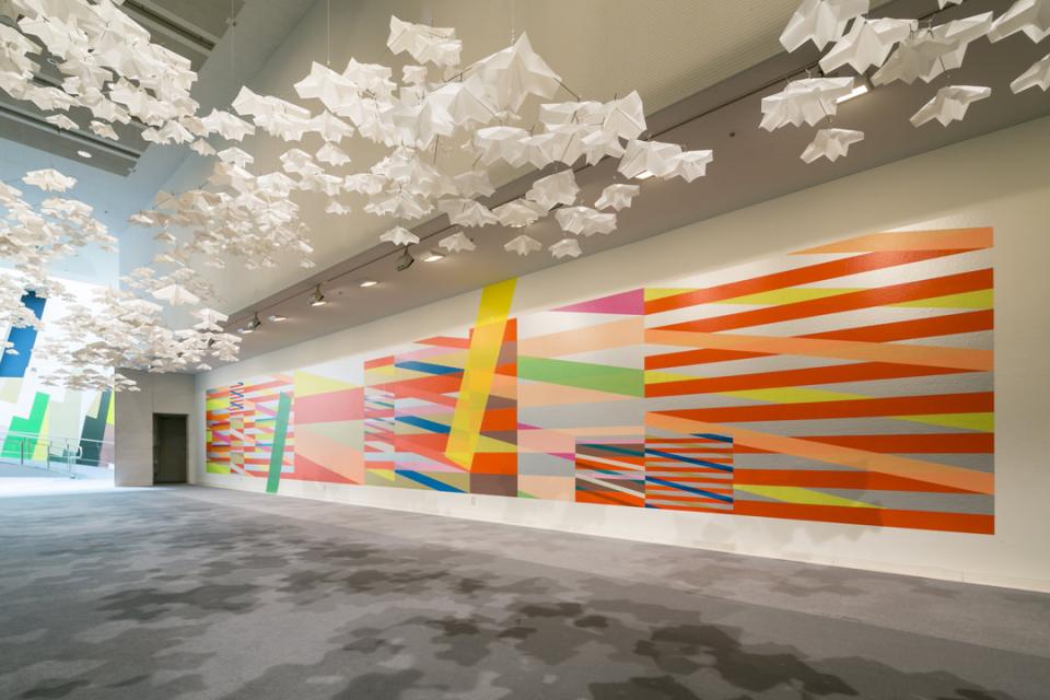 Vibrant mural featuring geometric patterns and colorful designs, alongside delicate origami-like hanging decorations for modern interior design.