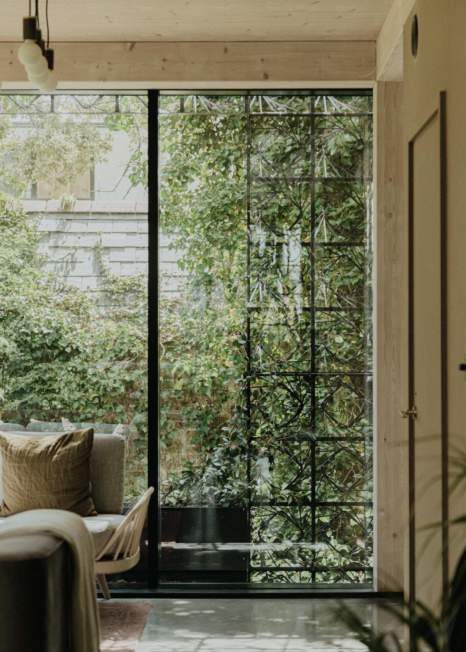 Modern living room with large glass windows showcasing lush greenery, highlighting the integration of nature in Giles Miller Studio's design.