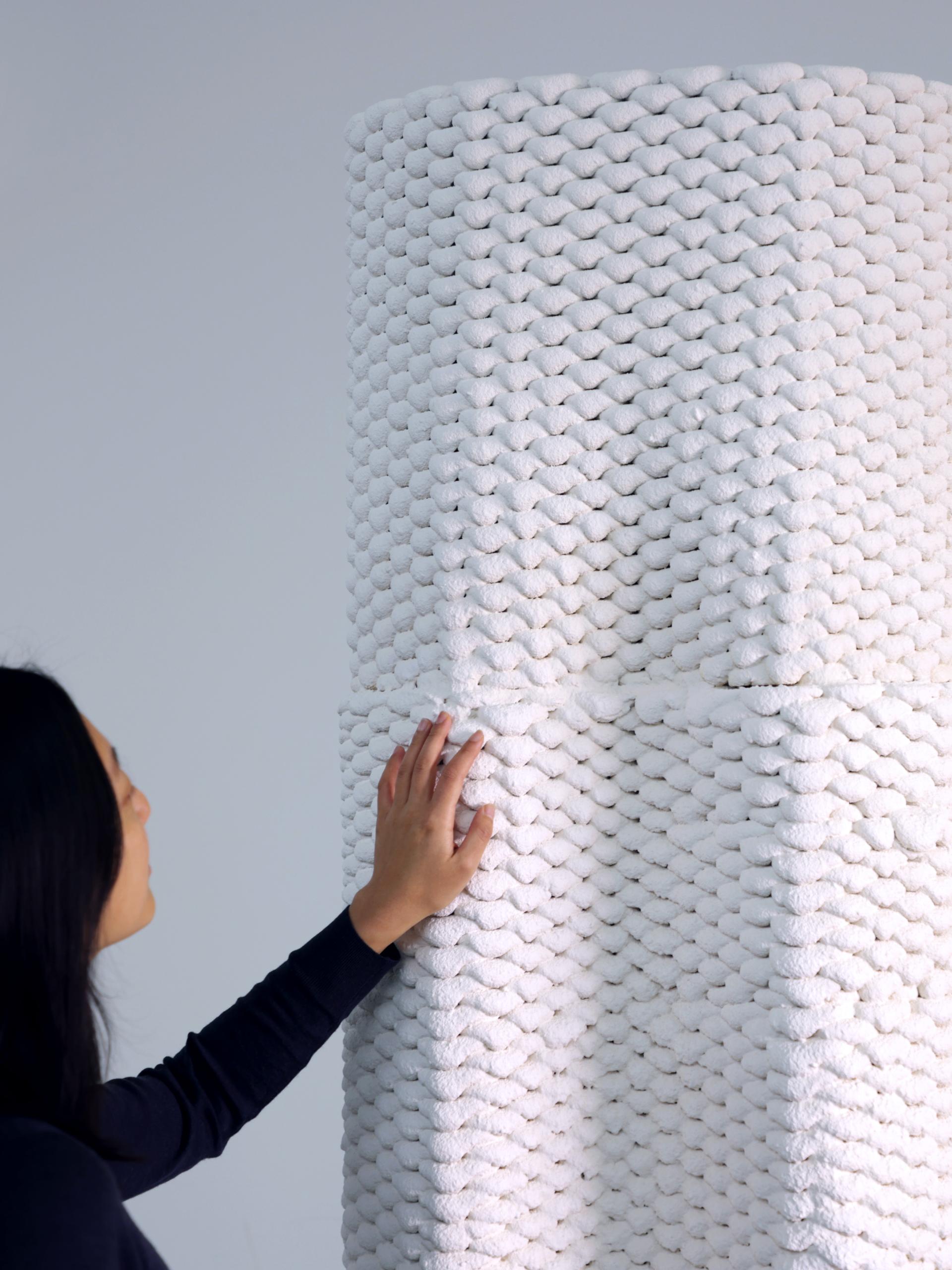 A person examines a textured, 3D printed structure made from white material, showcasing innovative construction techniques.