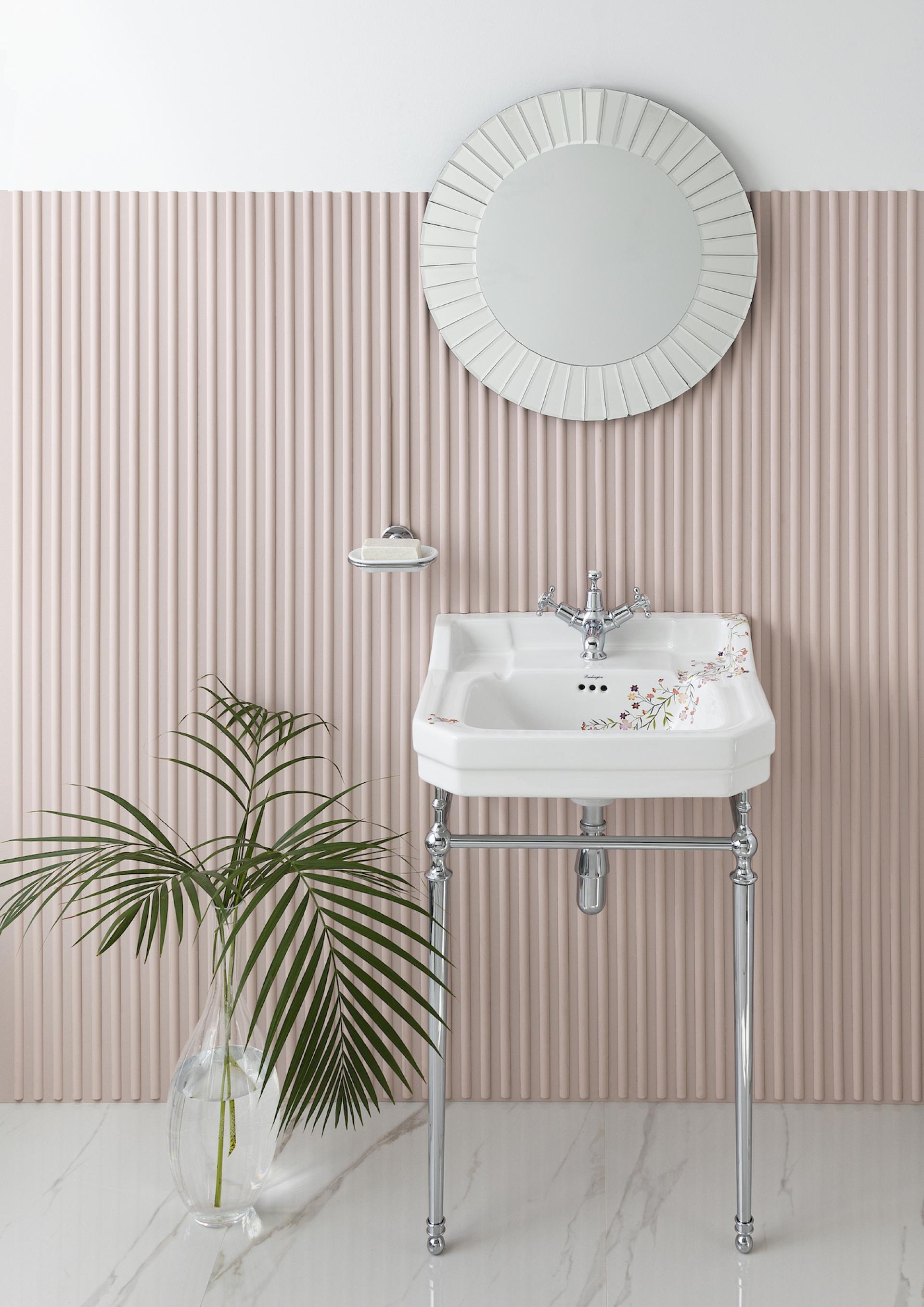 Stylish bathroom setup featuring a vintage sink, decorative mirror, and greenery against a textured pink wall.