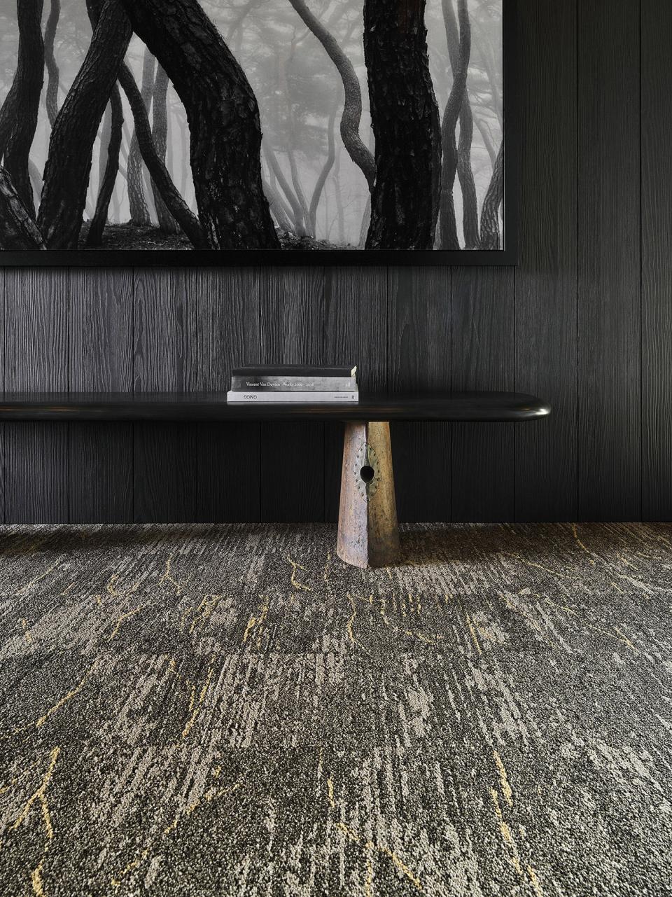 Modern interior featuring a rustic table, textured carpet, and a black and white nature artwork, embodying wabi-sabi aesthetics.