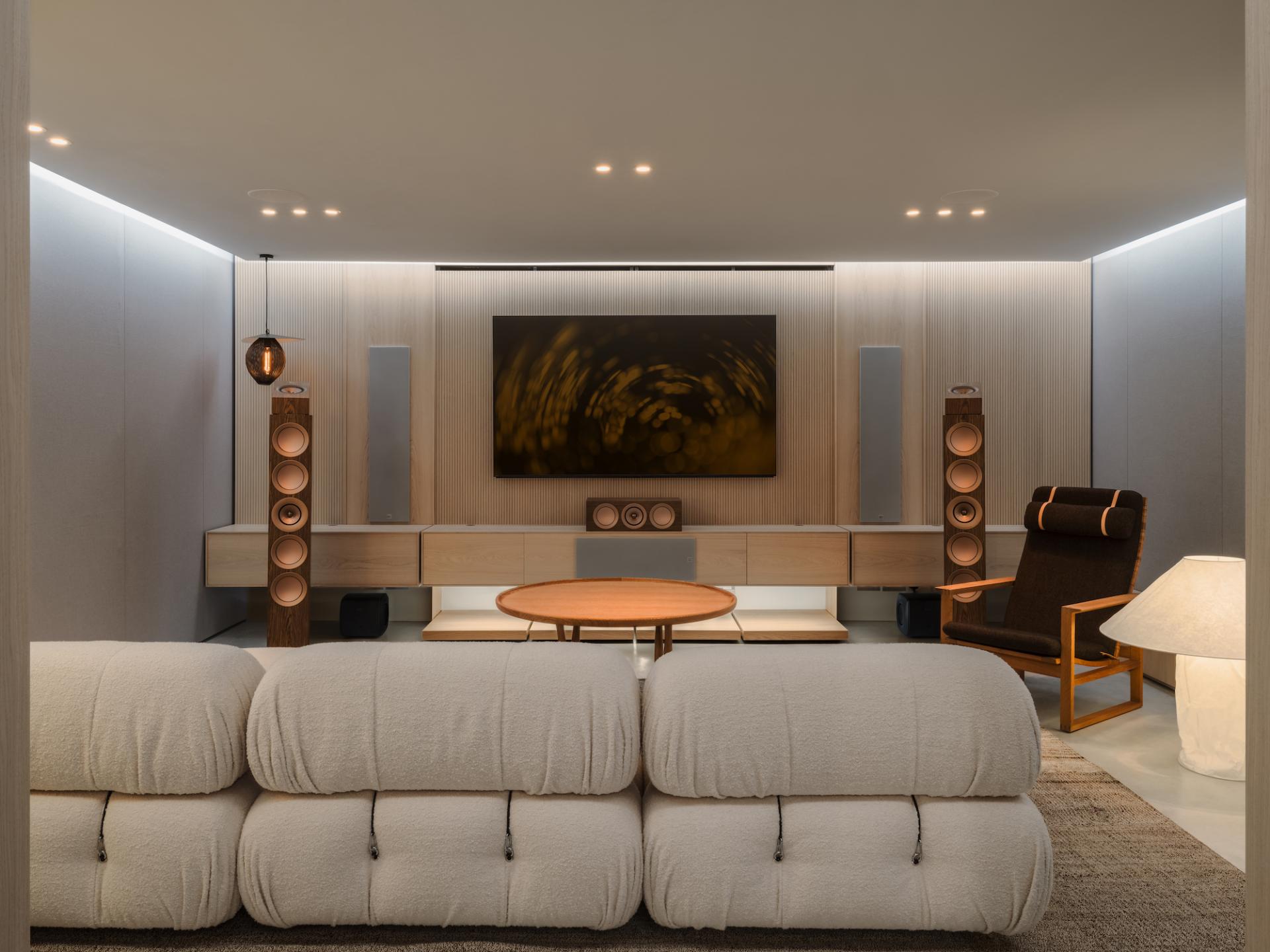 Modern audio room featuring KEF speakers, a stylish sofa, and a large wall-mounted TV in a sleek design.