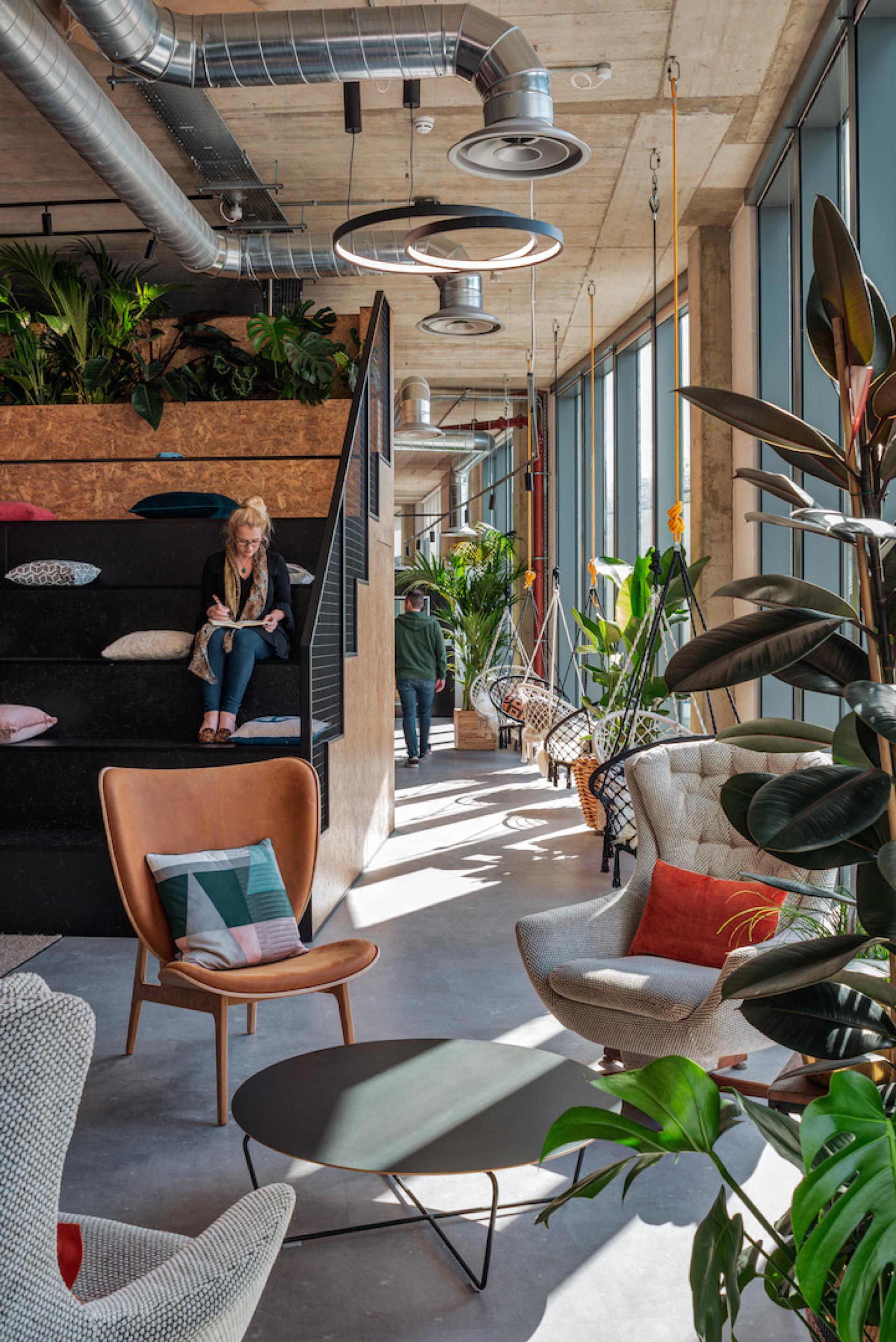 Modern workspace featuring creative seating, lush greenery, and a designer ambiance, reflecting sustainability and post-Covid design trends.