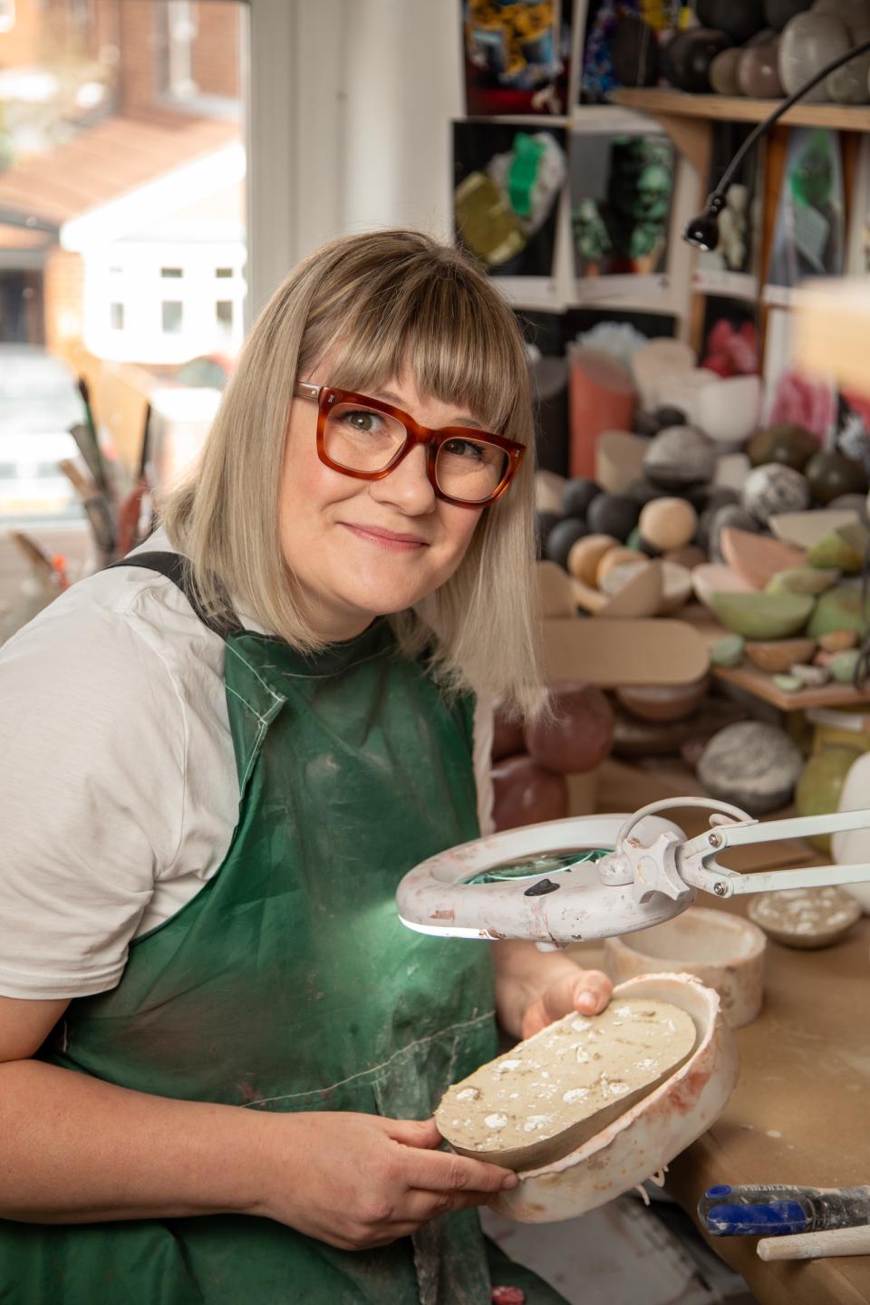 Sculptor Vic Wright in her studio, holding a piece of clay while surrounded by various sculpting materials.