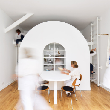 Flexible living space in a Parisian home, featuring an innovative circular bookshelf and active residents engaged in daily activities.