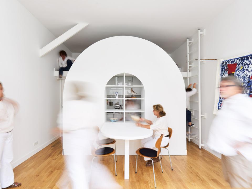 Flexible living space in a Parisian home, featuring an innovative circular bookshelf and active residents engaged in daily activities.
