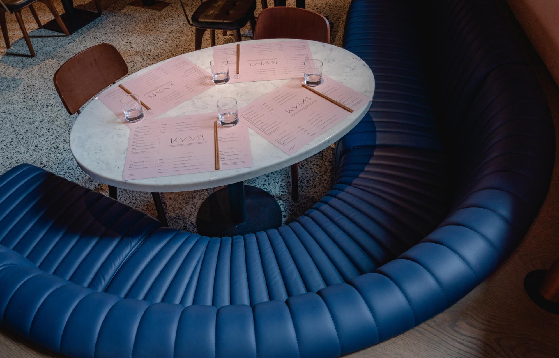 Stylish blue upholstered seating surrounds a marble table set with menus for Chef Andrew Wong's new restaurant.