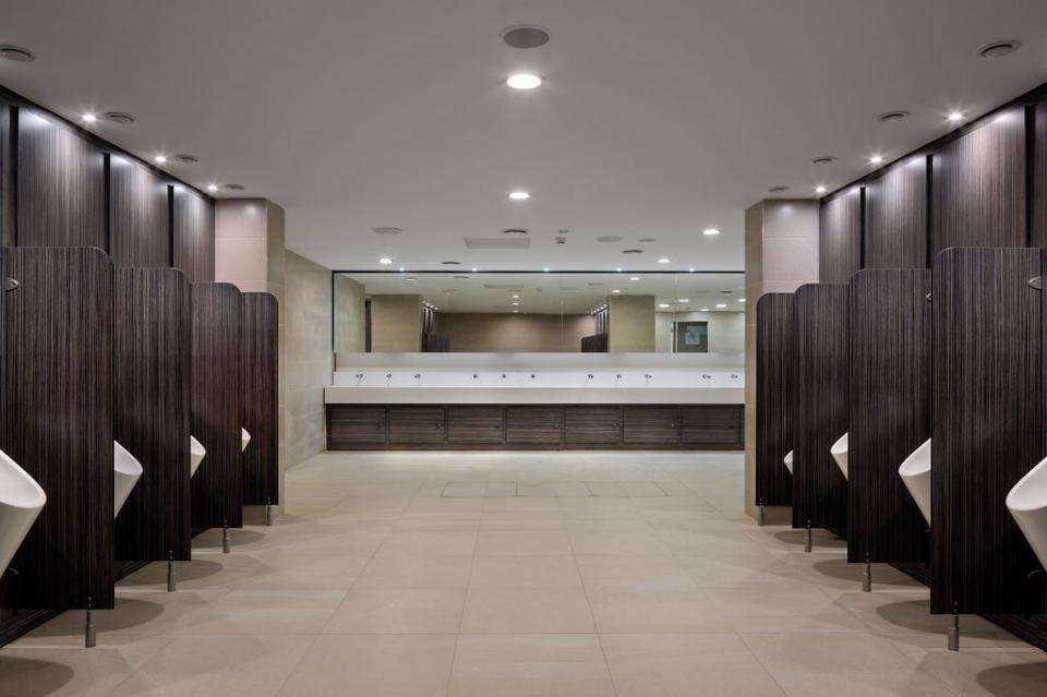 Modern washroom interior at Liverpool Street Station, featuring urinals, sinks, and stylish wood and tile finishes.