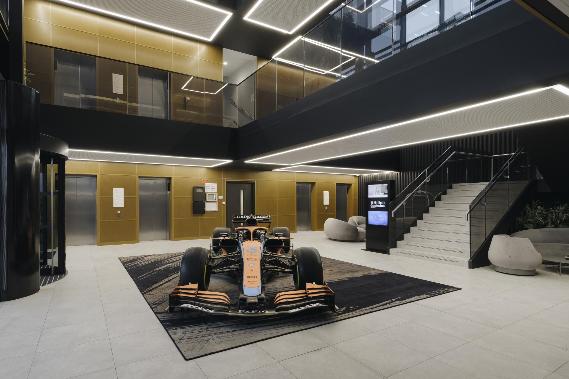 Modern commercial lobby featuring a McLaren Formula 1 car on a stylish rug, elegant furnishings, and sleek design elements.