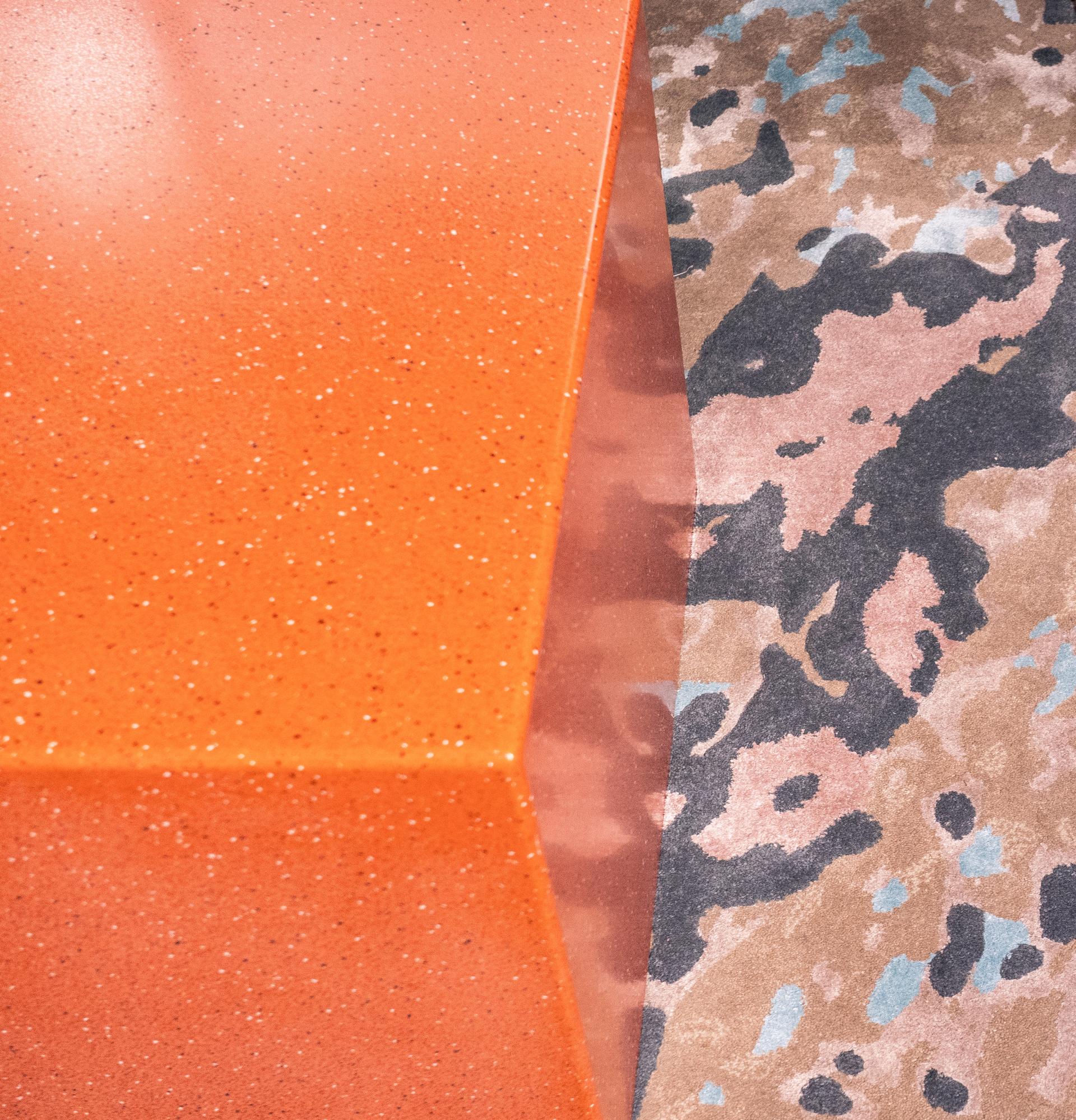 Bespoke rug featuring an organic, earthy color palette, paired with a vibrant orange surface in a modern interior.