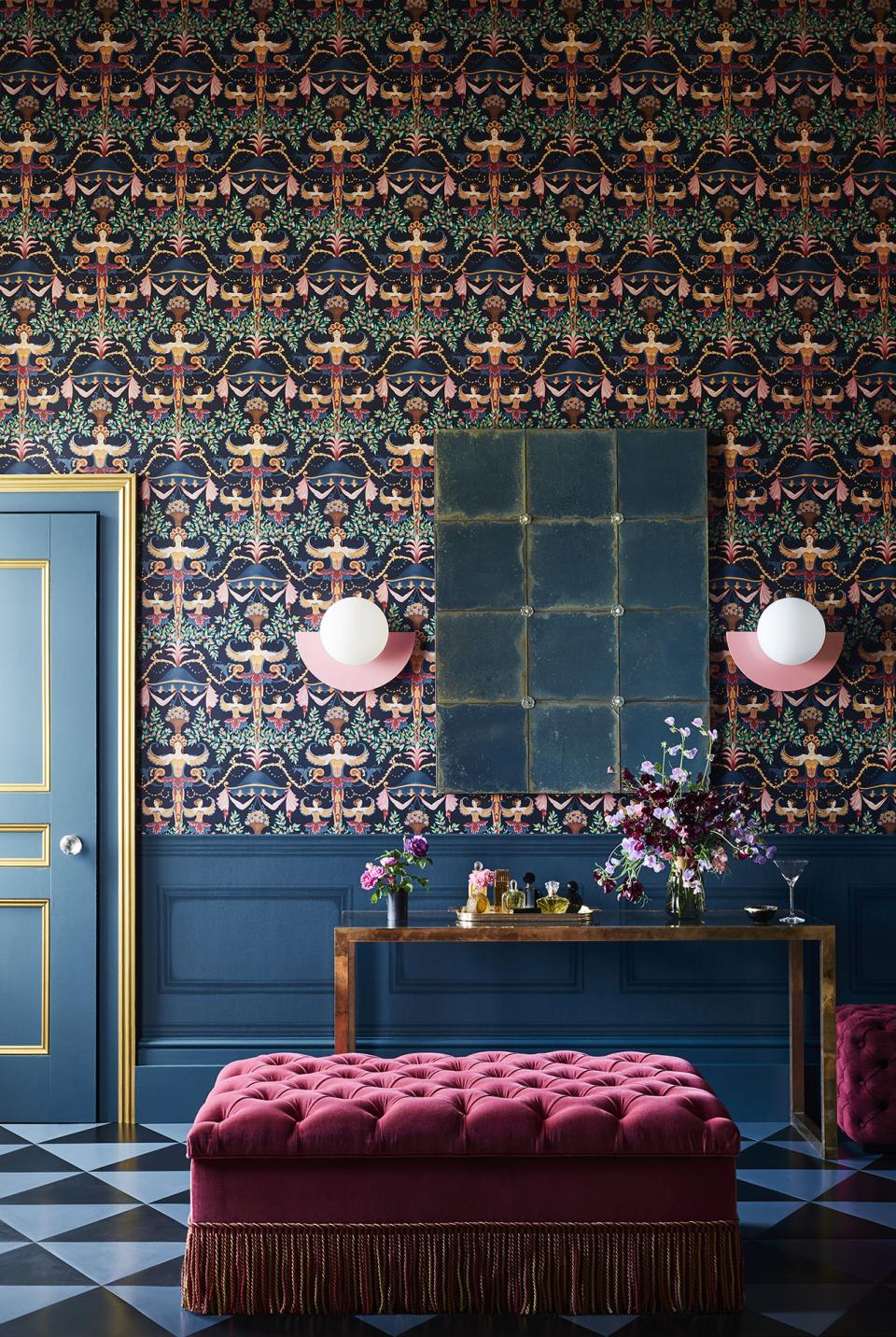 Vibrant interior featuring intricate Cole & Son wallpaper, a pink tufted ottoman, and a stylish console table with floral arrangements.