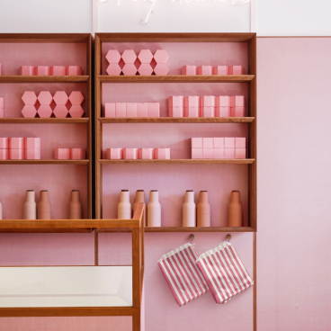 Bright pink shelves display pastel products with a neon "stay humble" sign, creating a modern, inviting retail atmosphere.
