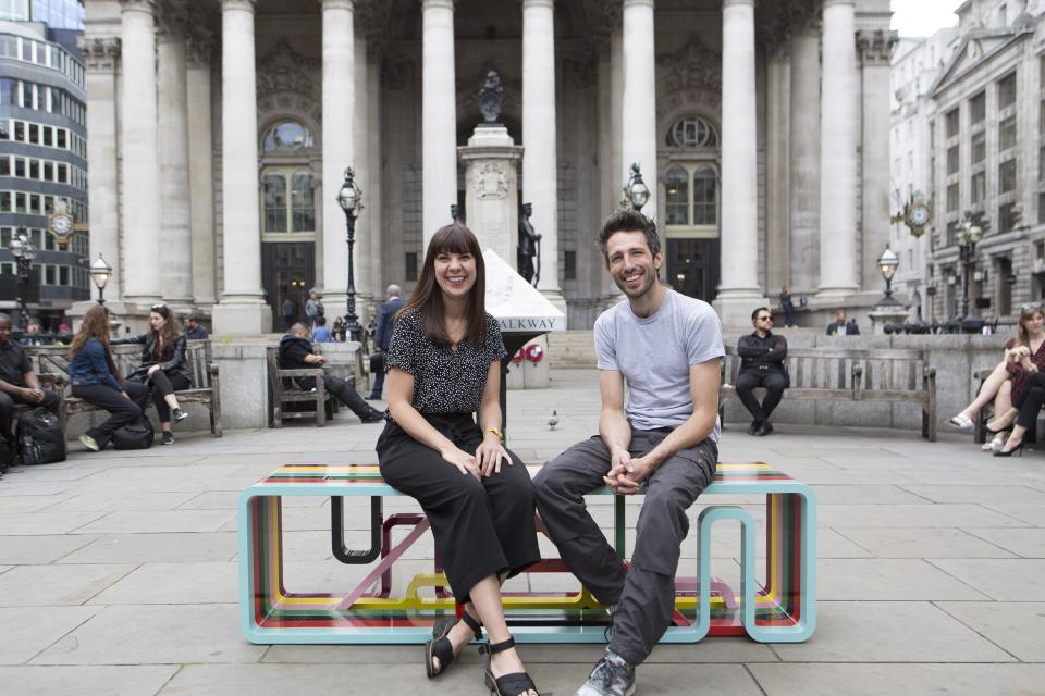 Two designer-makers seated on a colorful modern bench in an urban setting, highlighting contemporary design and craftsmanship.