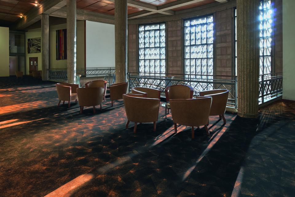 Modern interior featuring Forbo's Flotex By Starck floor covering, highlighting stylish brown chairs and natural light.