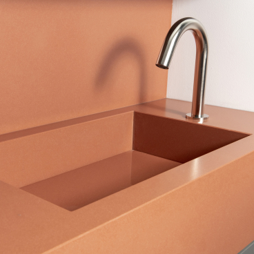 Sleek modern washroom sink with a polished faucet featured on a stylish coral-colored countertop.