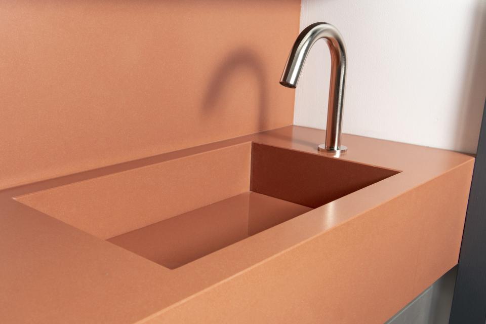 Sleek modern washroom sink with a polished faucet featured on a stylish coral-colored countertop.