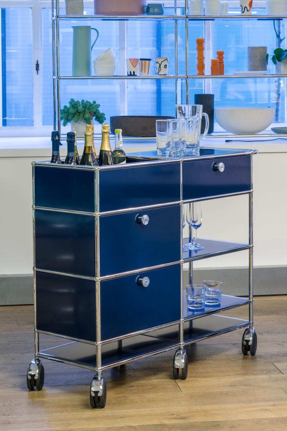 Stylish USM modular furniture serving cart in navy blue, featuring drawers, glassware, and decorative items in a showroom setting.