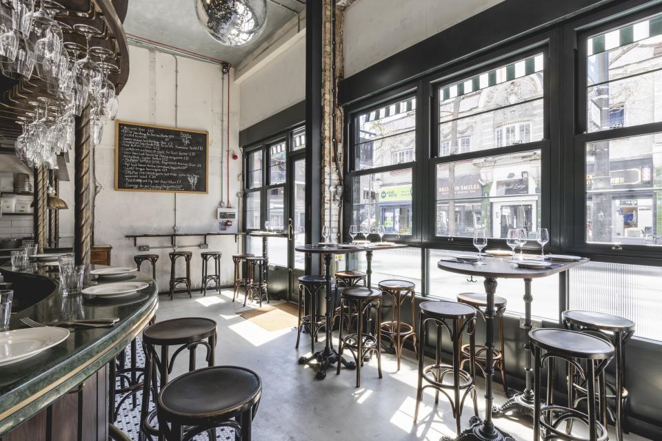 Bright and airy Parisian-inspired wine bar interior featuring sleek tables, bar stools, and large windows.