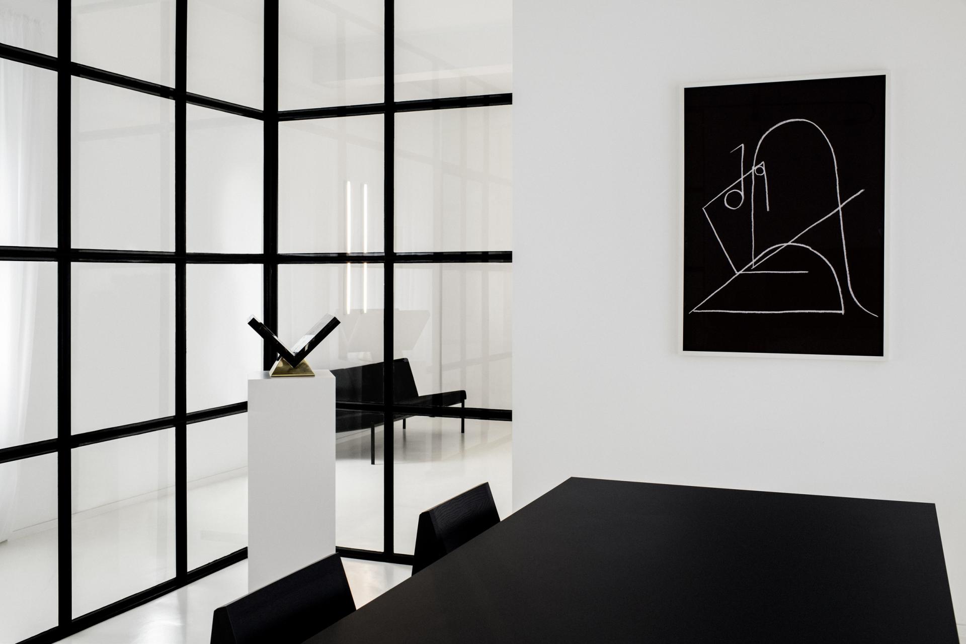 Modern interior design featuring a minimalist black table, geometric artwork, and sleek glass partitions in a Dusseldorf atelier.