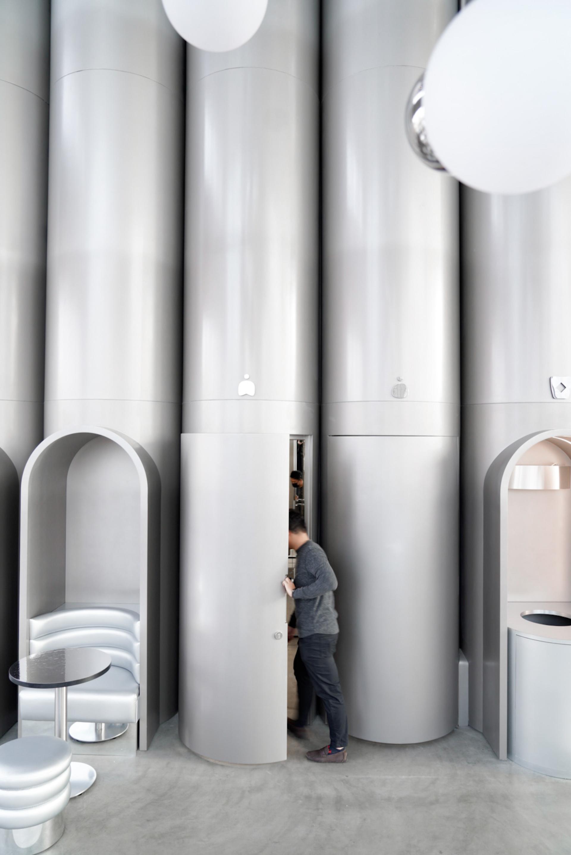 Modern interior of MO bakehouse featuring sleek metallic structures, a person interacting with cabinetry, and contemporary seating.