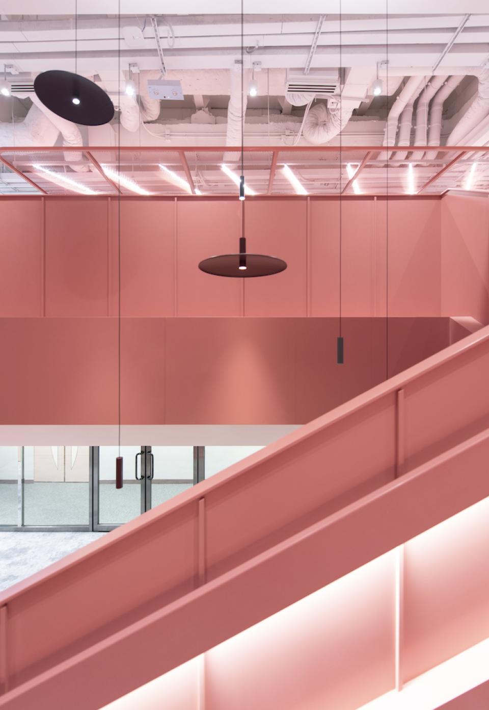 Modern pink workspace design featuring elegant lighting and an open stairway at Jardine Restaurant Group by Bean Buro.