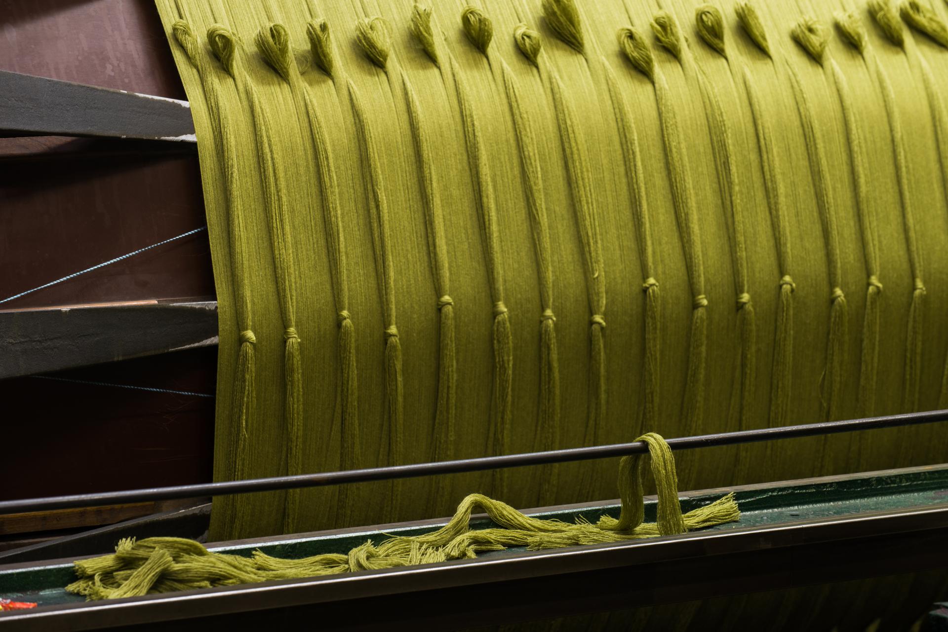 Thick green yarn strands are neatly arranged on a textile machine, showcasing Bute's craftsmanship in materials.