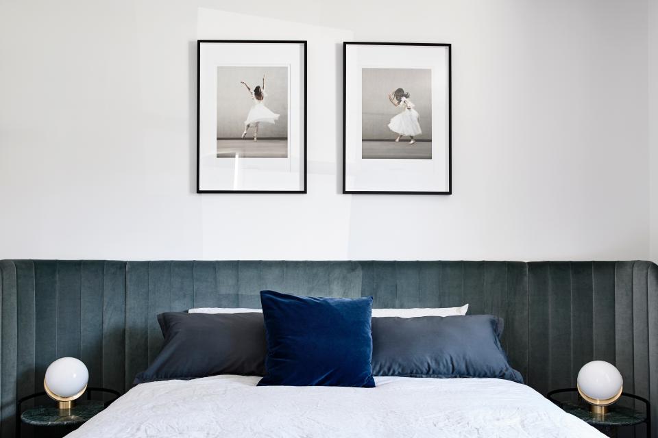 Elegant bedroom featuring a velvet headboard, decorative pillows, and framed ballet photos, showcasing Parisian-inspired design.