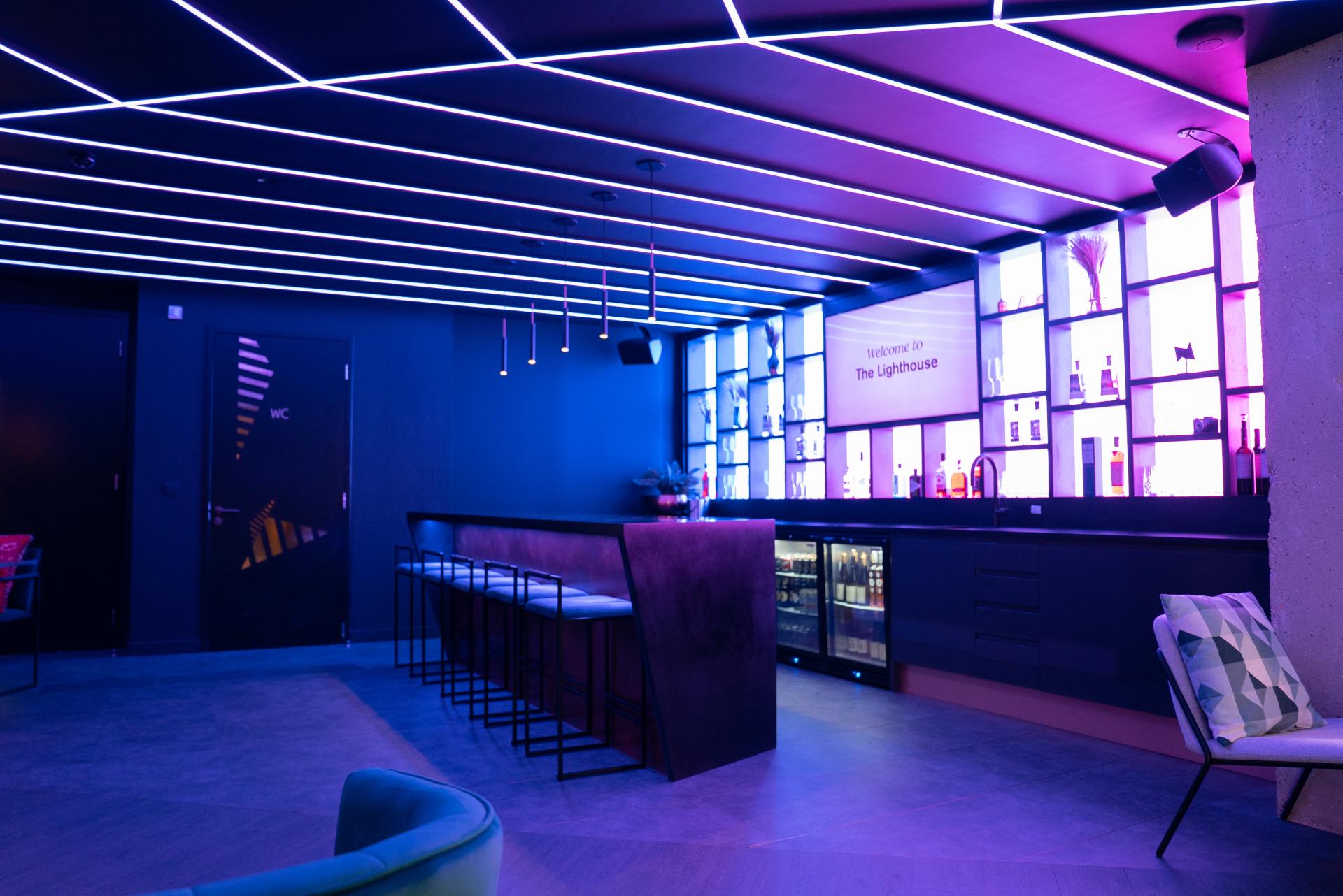 Futuristic bar interior of The Lighthouse showroom, featuring ambient lighting, a sleek counter, and colorful decorative shelves.